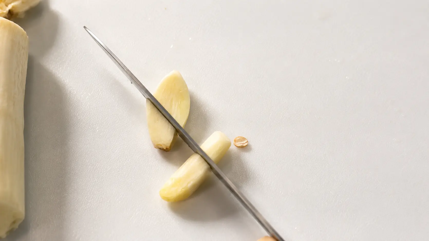 Fresh garlic cloves being sliced on a white cutting board for cheesy Shin ramen noodles.