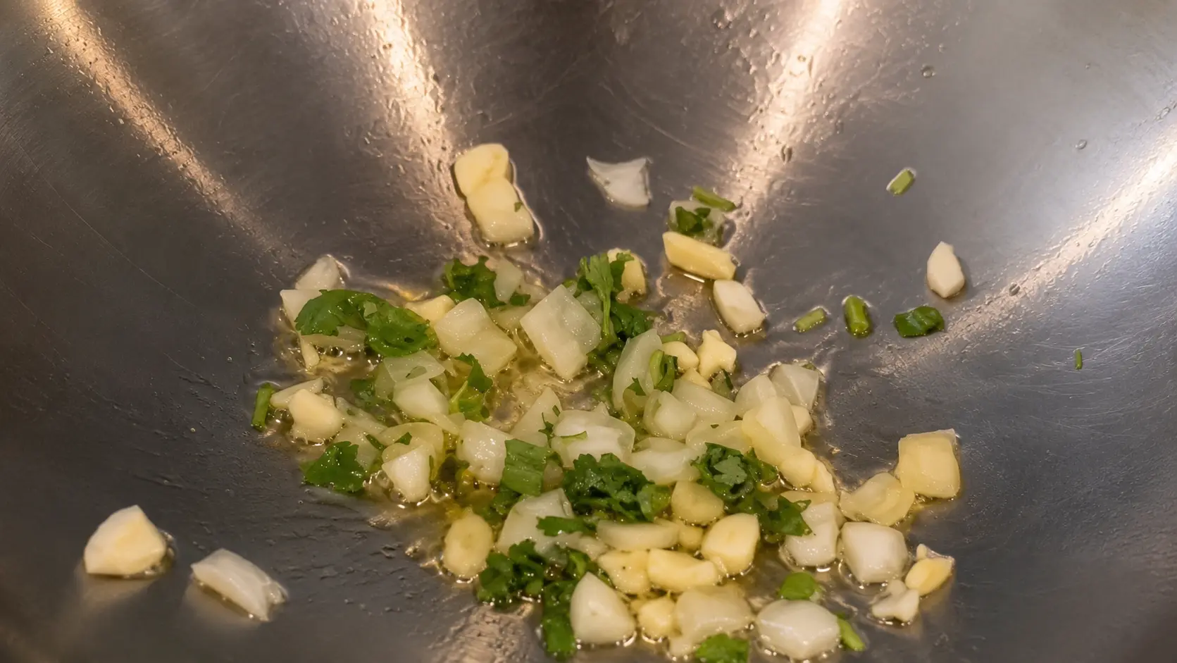 Garlic, onion, and fresh cilantro sautΓ©ing in oil in a wok for cheesy Shin ramen noodles.