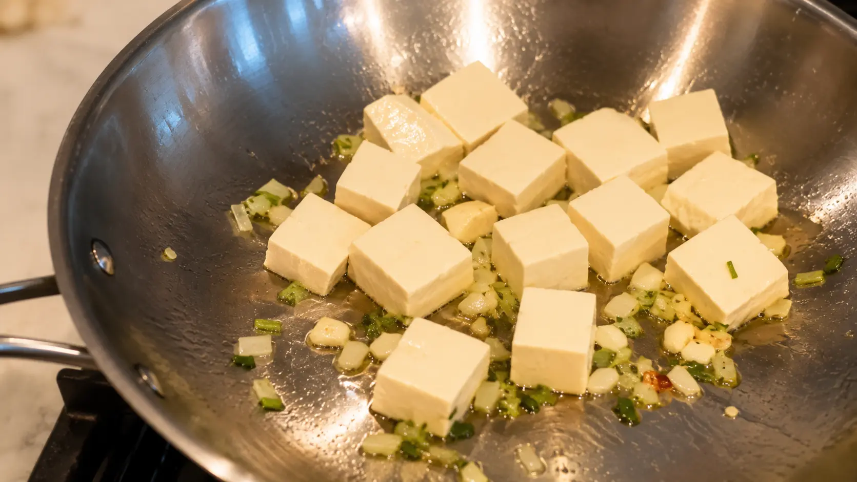 Tofu cubes sautΓ©ing with garlic, onion, and herbs in a wok for cheesy Shin ramen noodles.
