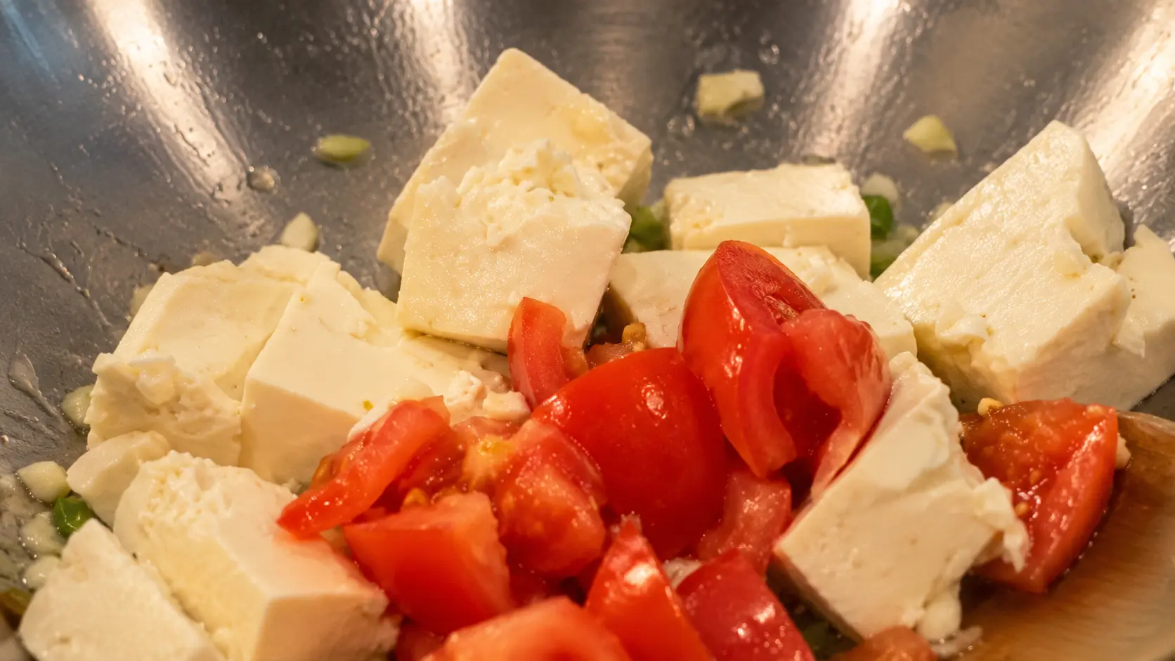 Fresh diced tomatoes and tofu cooking in a wok for cheesy Shin ramen noodles.