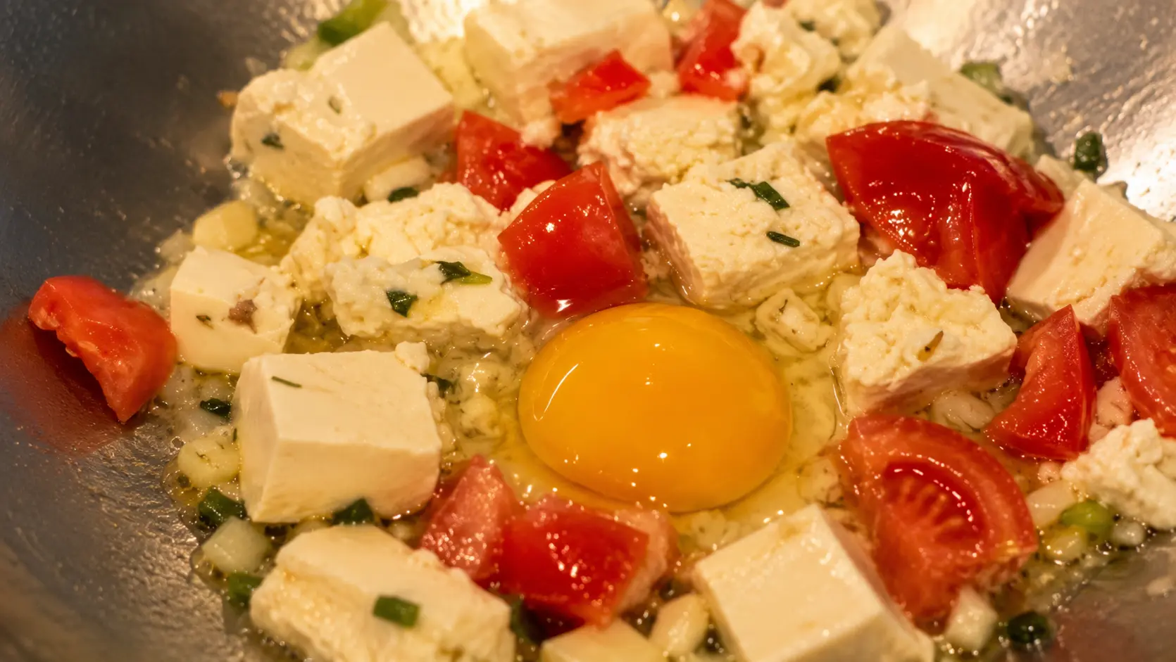 Egg yolk, tofu, and fresh tomatoes cooking in a wok for cheesy Shin ramen noodles.