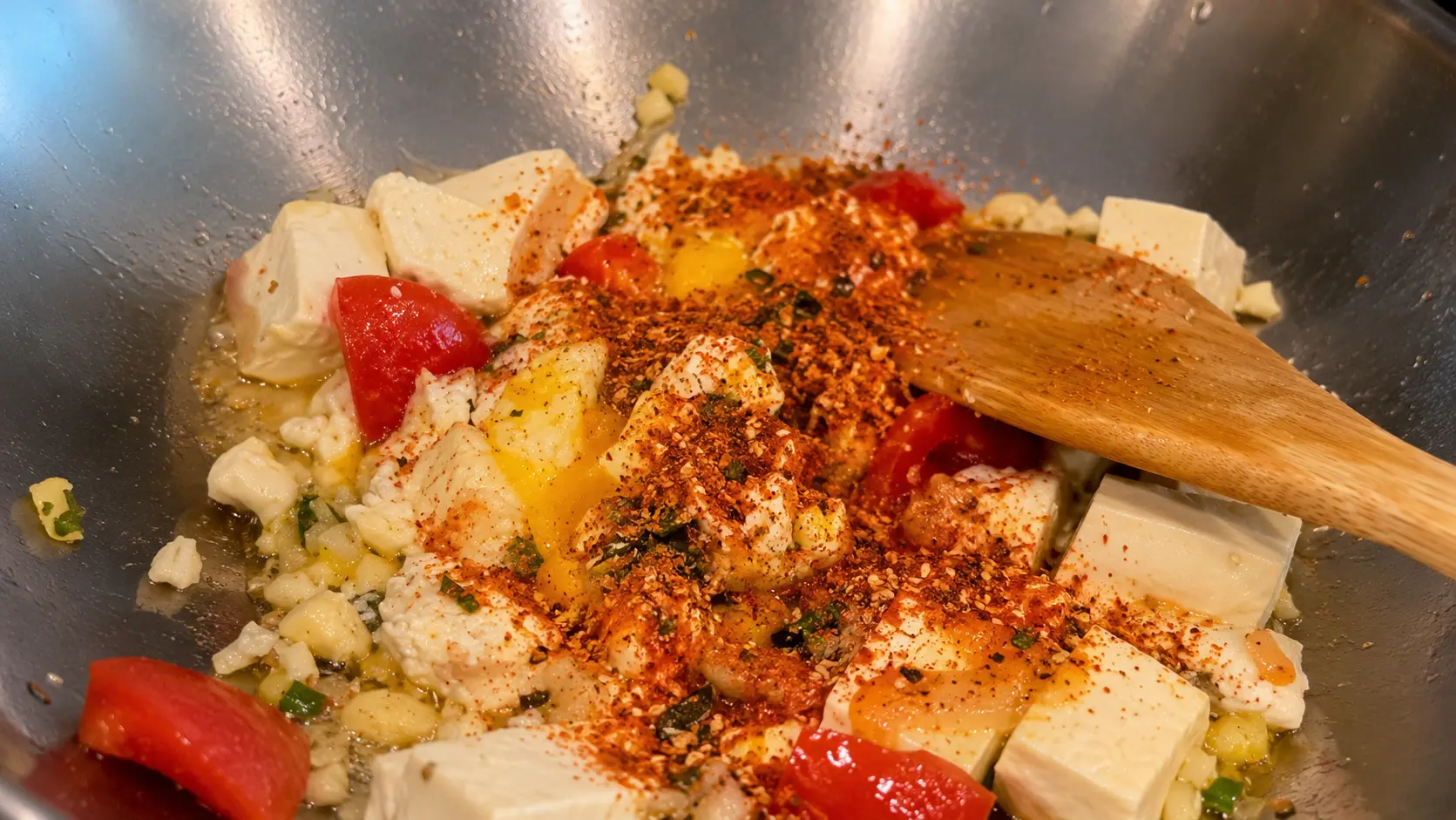 Shin ramen seasoning added to tofu, egg, and tomatoes in a wok for cheesy Shin ramen noodles.