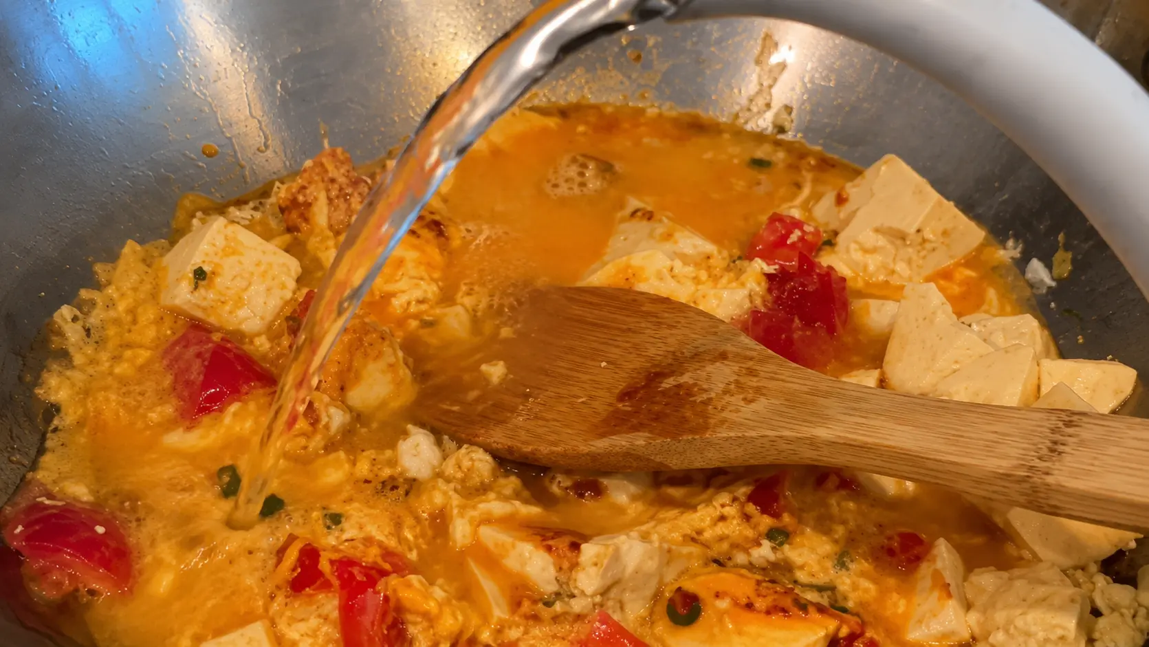 Water added to tofu, egg, and tomatoes in a wok to make cheesy Shin ramen noodles.