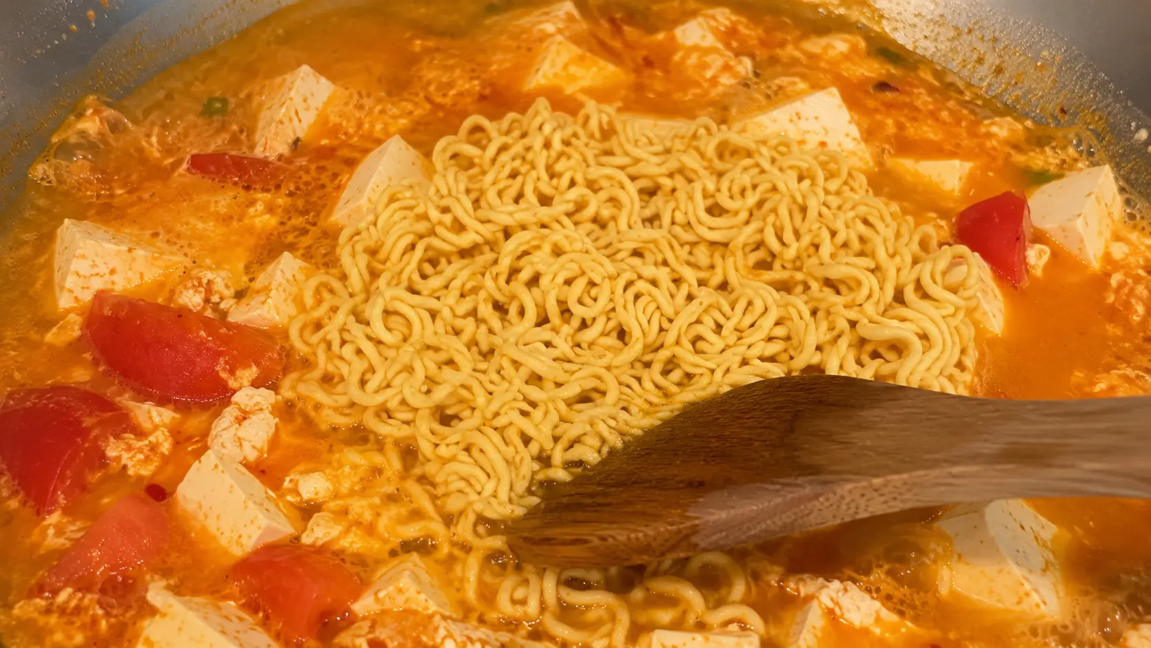 Shin ramen noodles simmering with tofu, tomatoes, and egg in a creamy spicy broth.