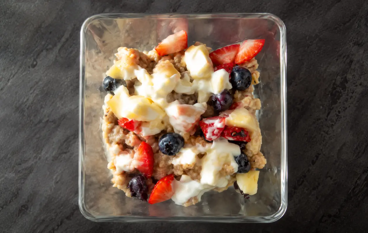 Creamy protein oatmeal topped with fresh strawberries, blueberries, banana, Greek yogurt, and honey in a glass bowl.