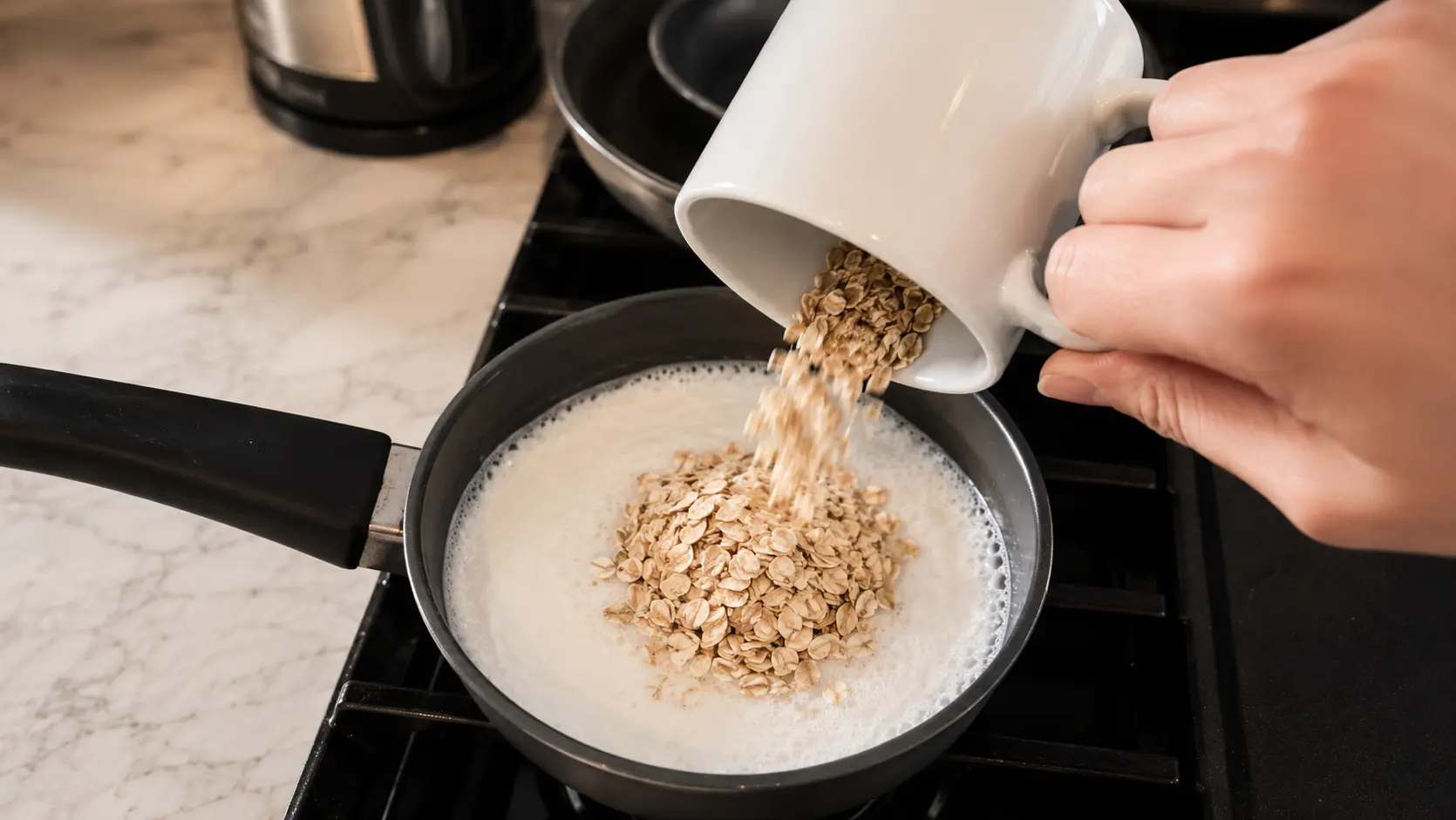 Rolled oats being poured into boiling milk in a saucepan on the stovetop to make creamy homemade protein oatmeal.