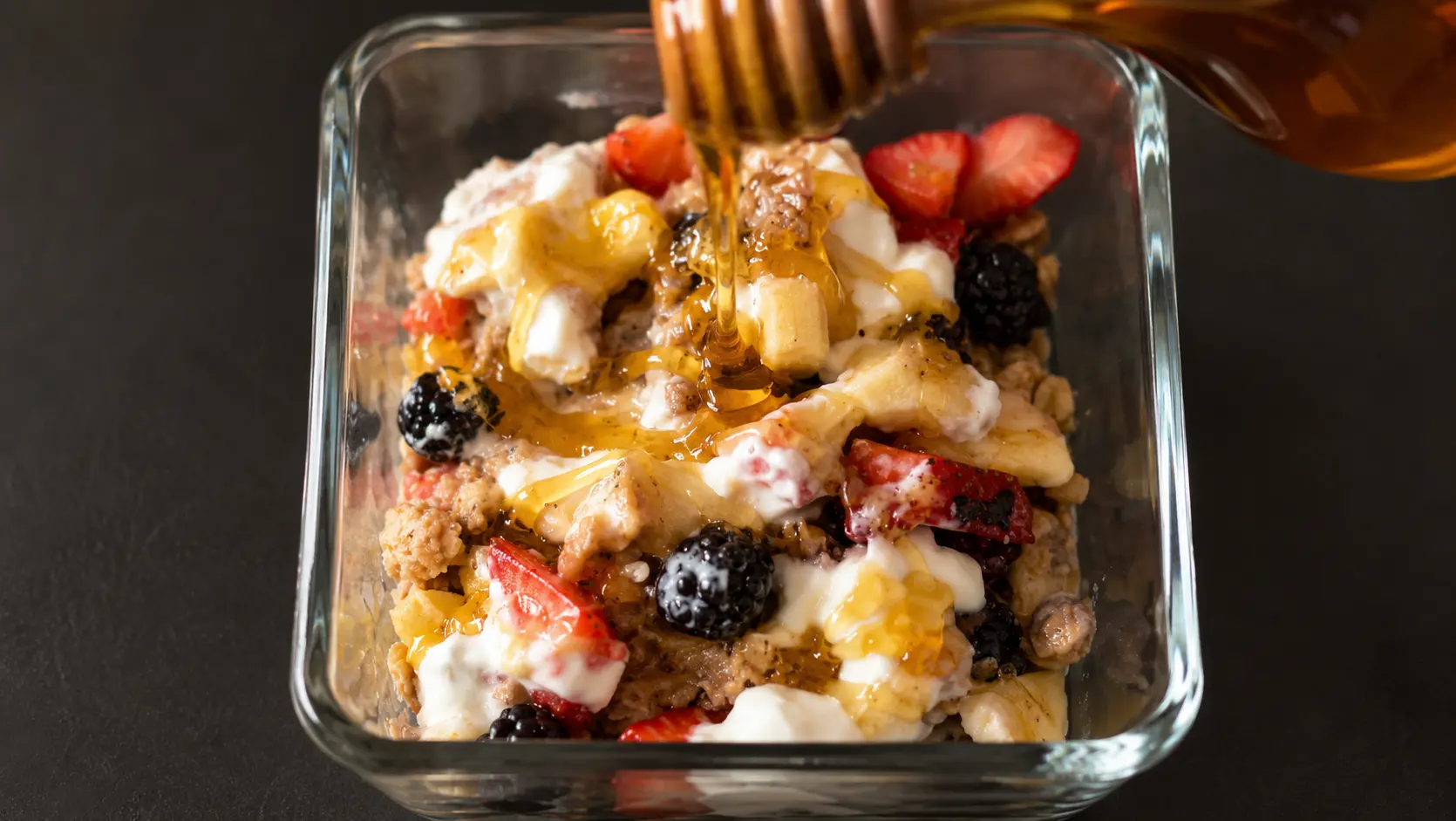 honey being drizzled on top of oatmeal with yogurt and fruits