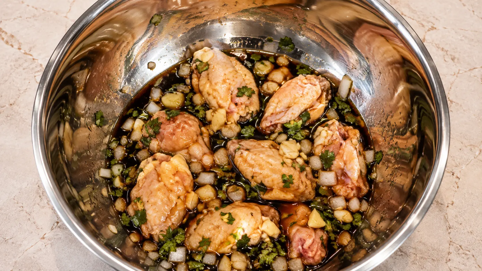 Raw chicken wings marinating with soy sauce, onion, garlic, and cilantro in a mixing bowl.