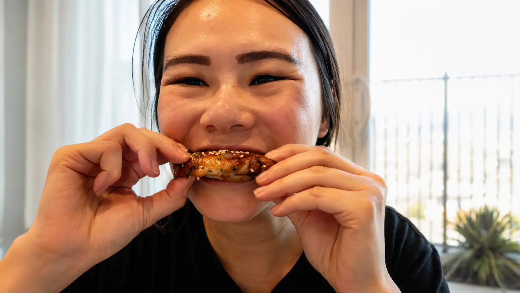 **Person taking a bite of a juicy teriyaki chicken wing during a taste test indoors.**