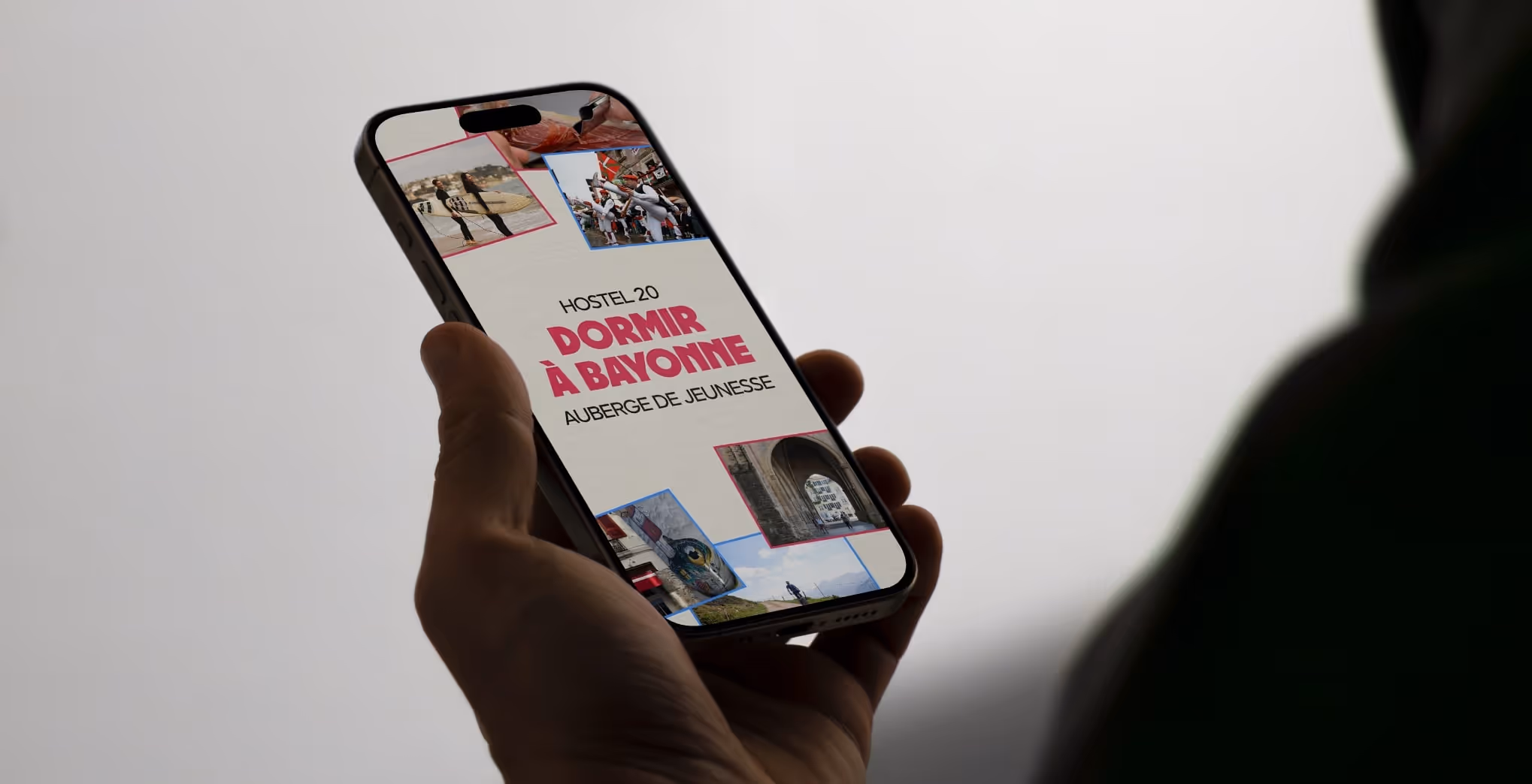 Main d'une personne tenant un smartphone affichant une page du site internet de Hostel 20 créé par le Studio Edoras pour une auberge de jeunesse.