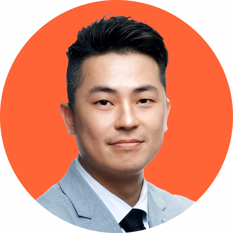 Portrait of a man with short black hair wearing a light gray suit, white shirt, and black tie, against an orange circular background.