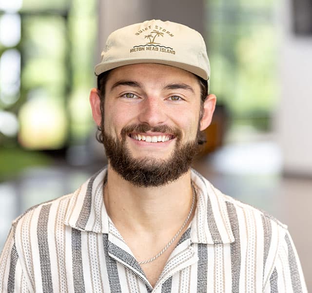 A man wearing a hat and smiling with neutral background.