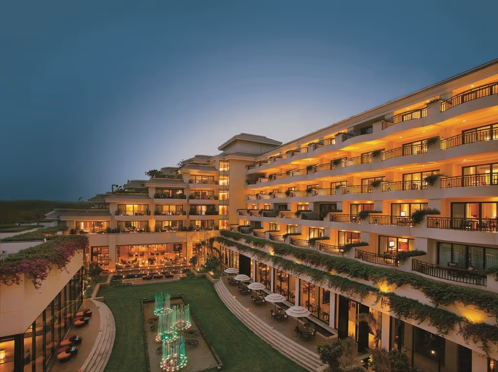 Evening view of a modern hotel with lit balconies and a garden featuring illuminated water fountains.