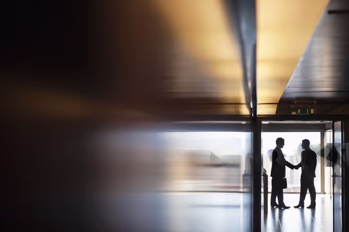 Two silhouettes of people shaking hands in a corridor
