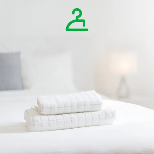 Two neatly folded white towels on a bed with a green clothes hanger icon above.