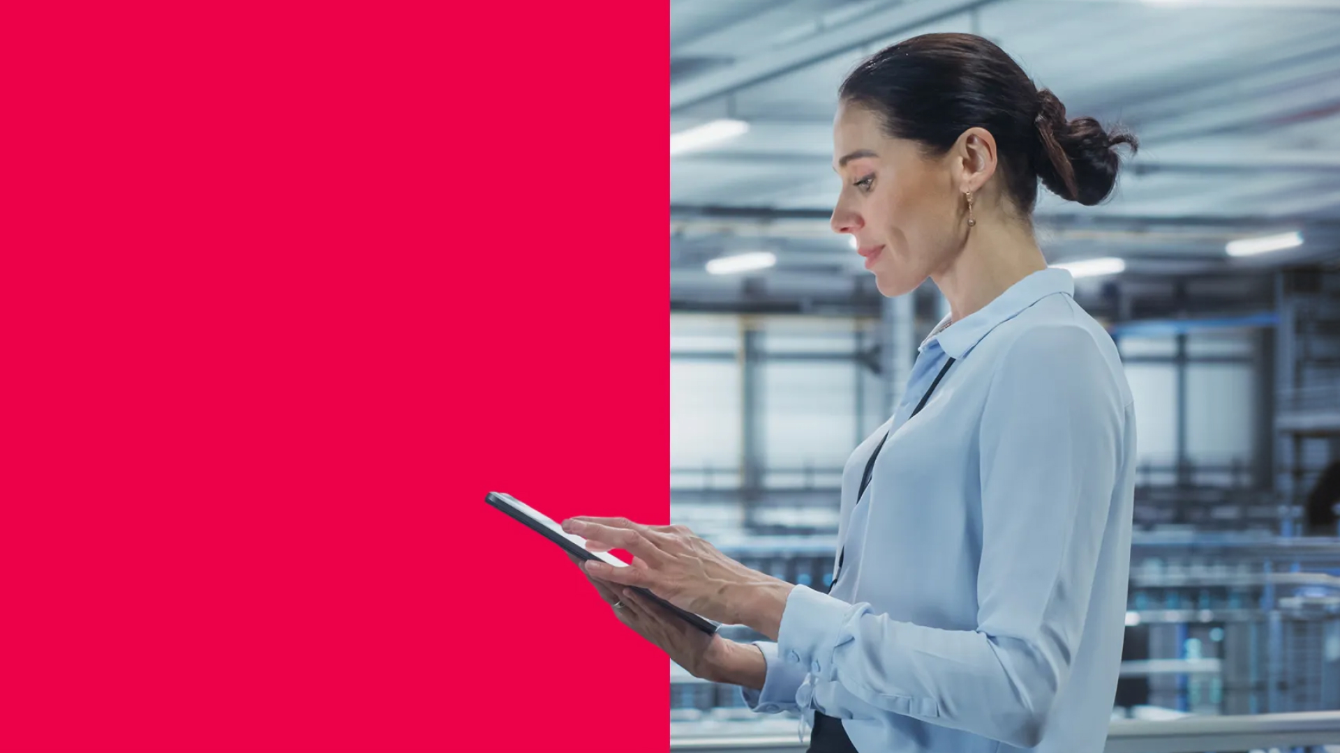 Alt-Text: Seitenansicht einer professionell gekleideten Frau in einer hellblauen Bluse, die ein Tablet benutzt, in einer modernen Industrie- oder Technikhalle; links im Bild befindet sich eine große rote Farbfläche.