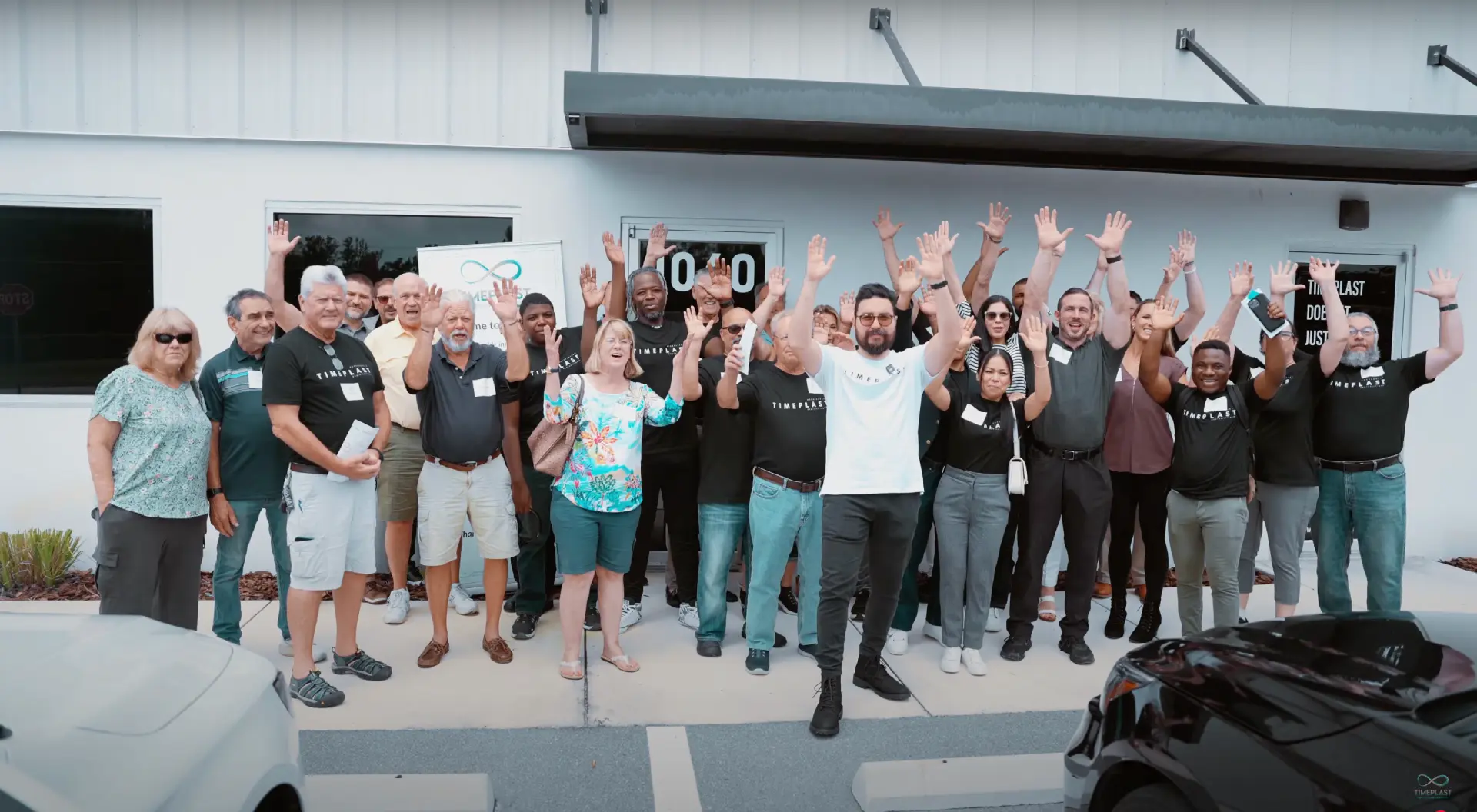 An enthusiastic group of people wave energetically in front of their office building entrance.