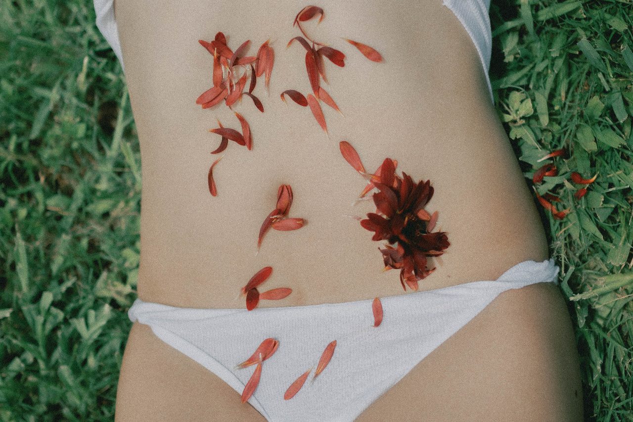 Red flower petals resting on a woman's abdomen, representing menstruation and iron loss