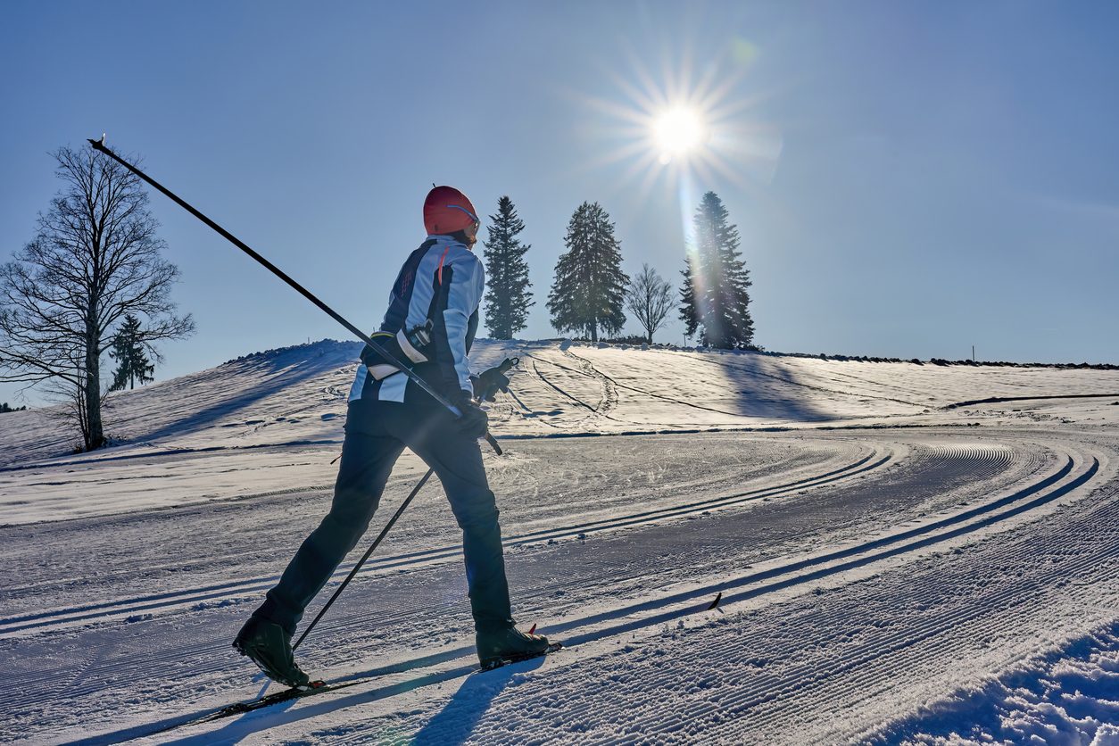 Cross-country skier gliding on a sunny groomed trail — staying active in winter