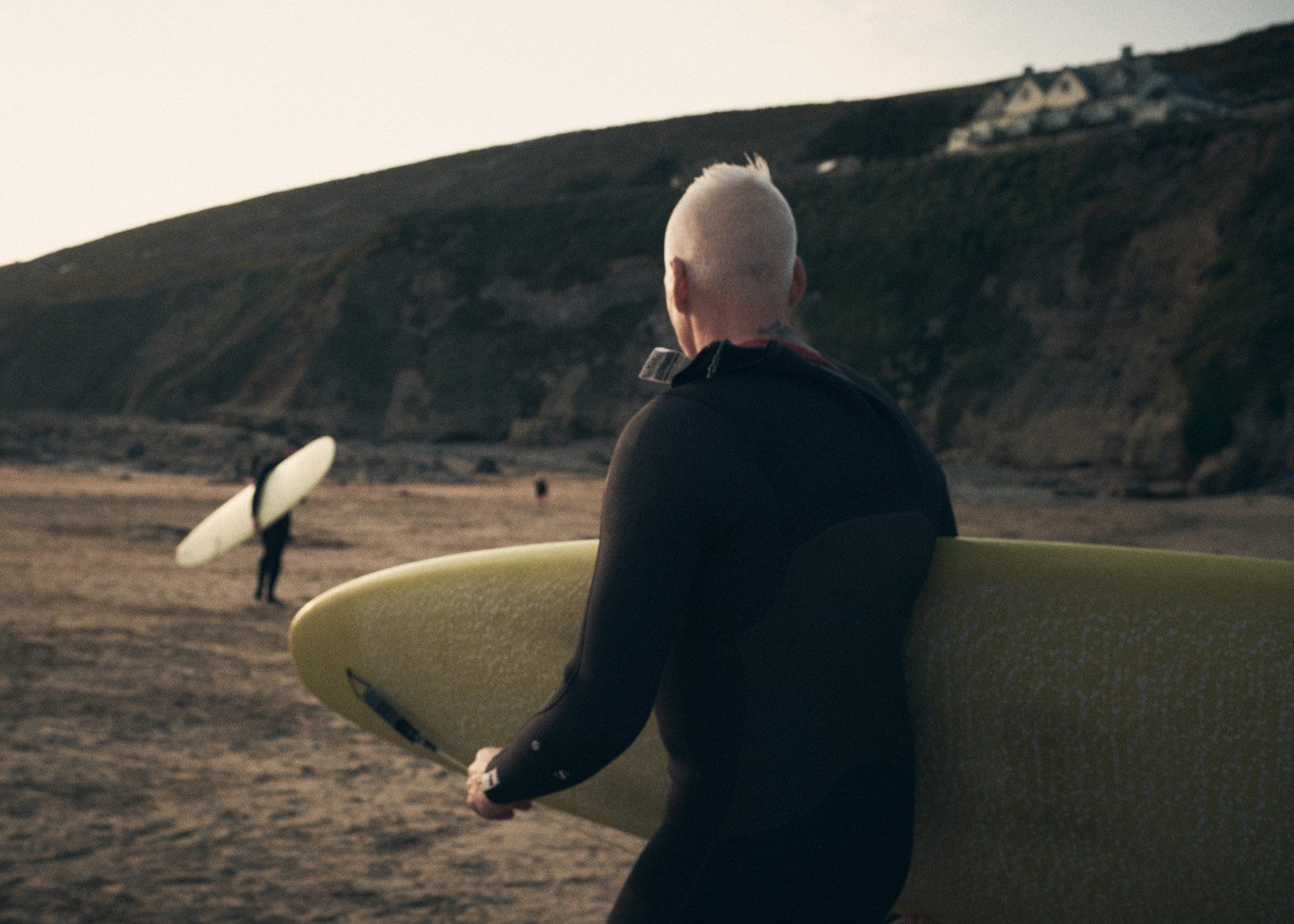 A surfer in a wetsuit carrying a board on the beach — staying active without joint pain