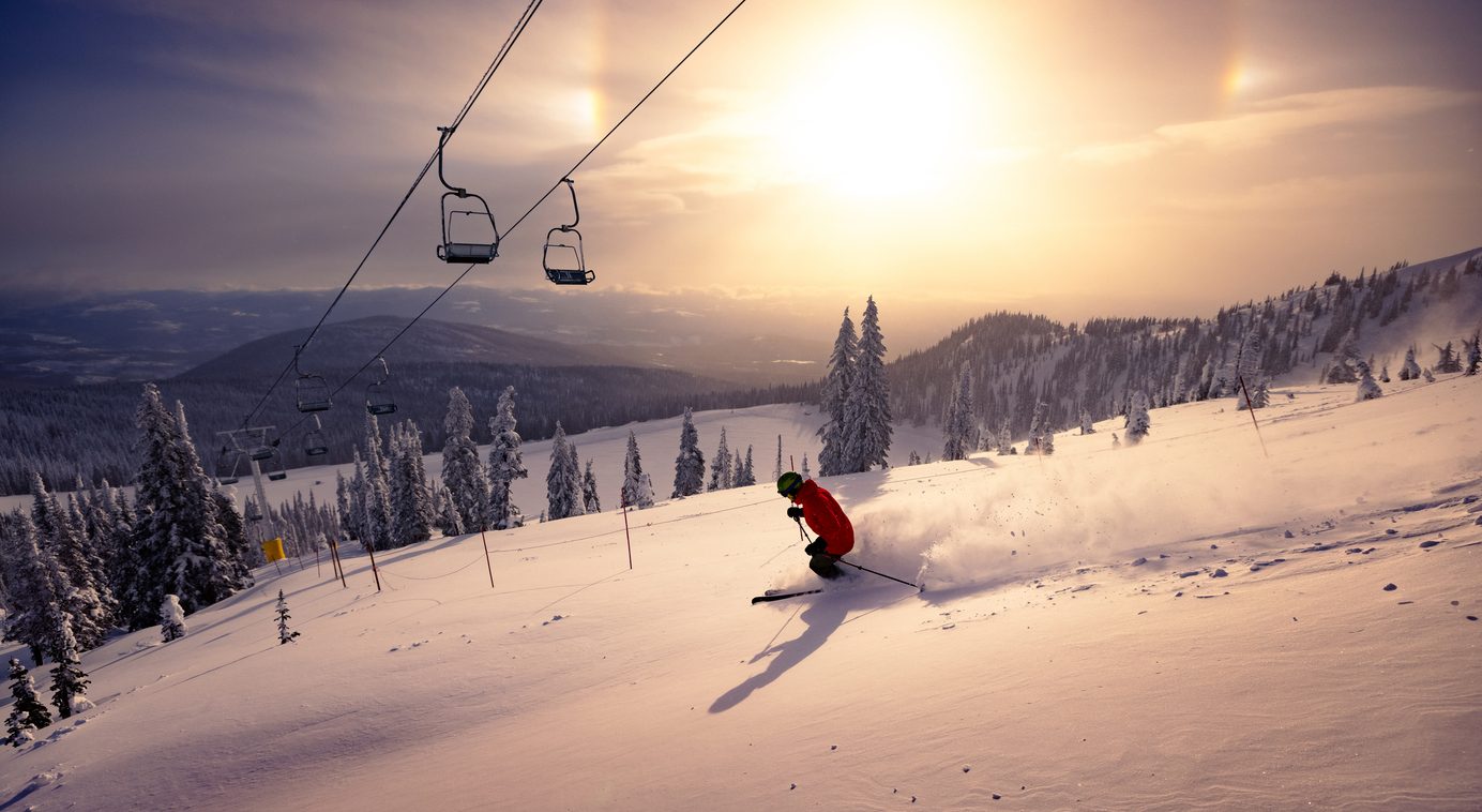 A skier carving downhill in fresh snow at sunrise — staying active with healthy knees