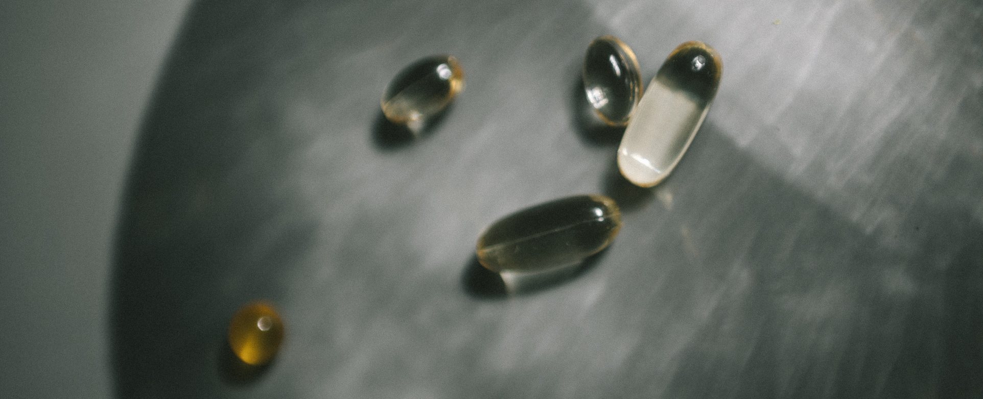 Fish oil and vitamin softgel capsules resting on a dark metal spoon