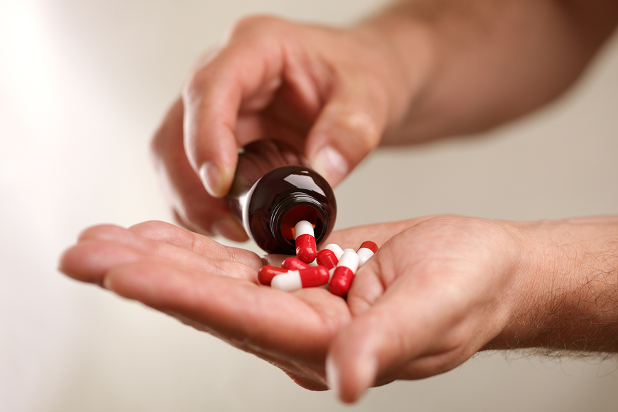 A hand of a person suffering from drug-induced neuropathy pouring red and white capsules from a bottle.