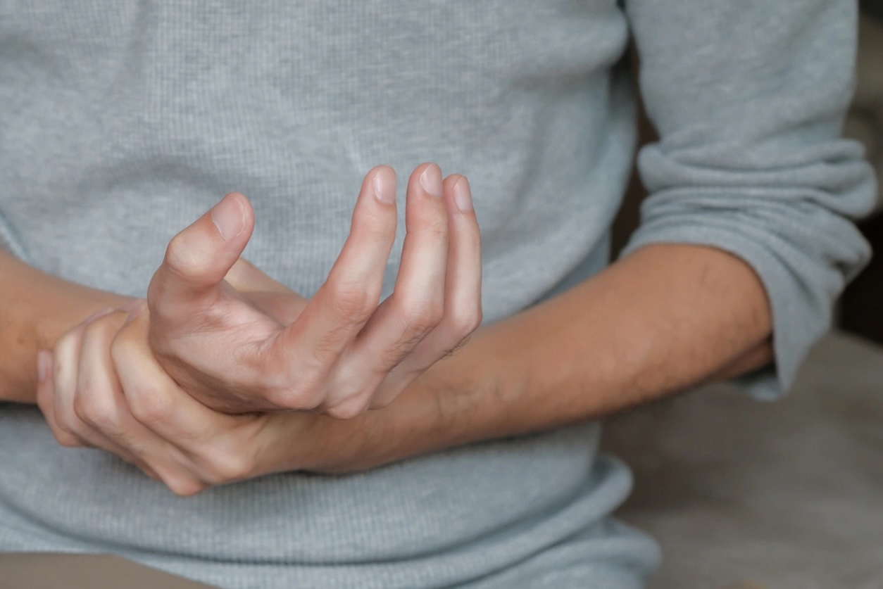 A man clutching his hand, showing wrist pain symptoms or peripheral neuropathy after alcohol detoxification.