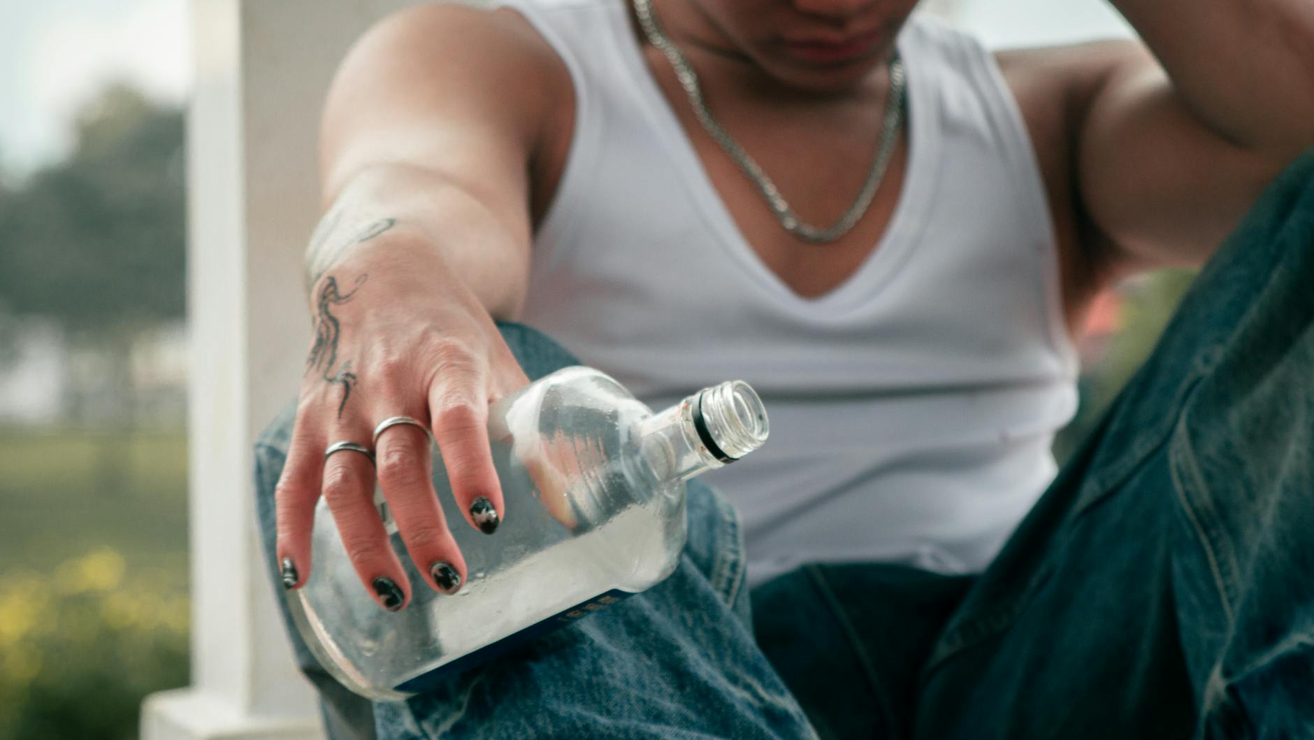 Person with tattoo holding empty liquor bottle, sign of alcohol withdrawal and showing symptoms of neuropathy.