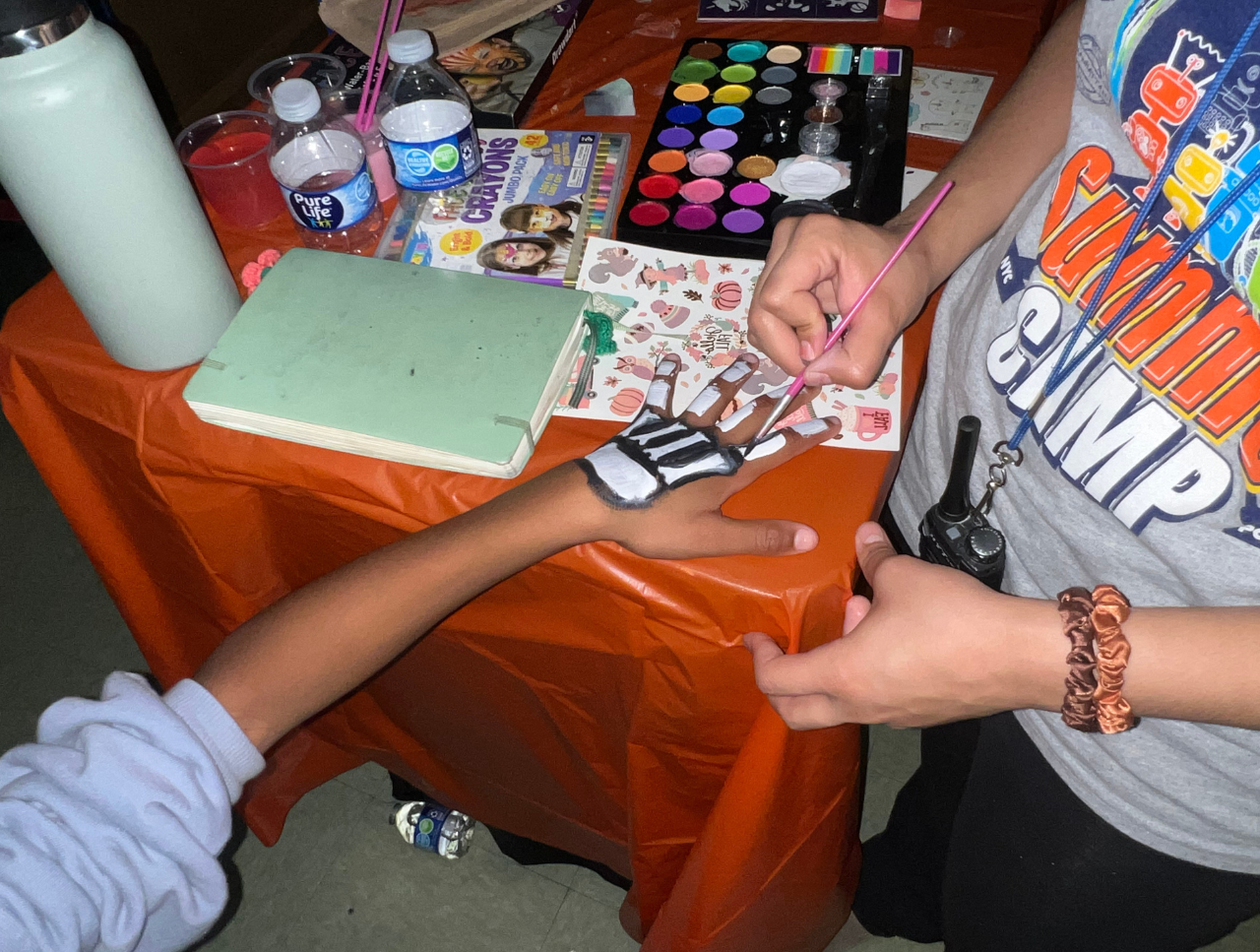 Camp counselor painting skeleton design on student's hand at activity table