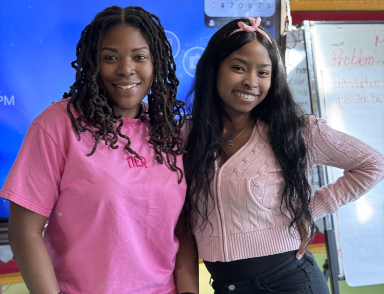 Two smiling students posing together in a classroom