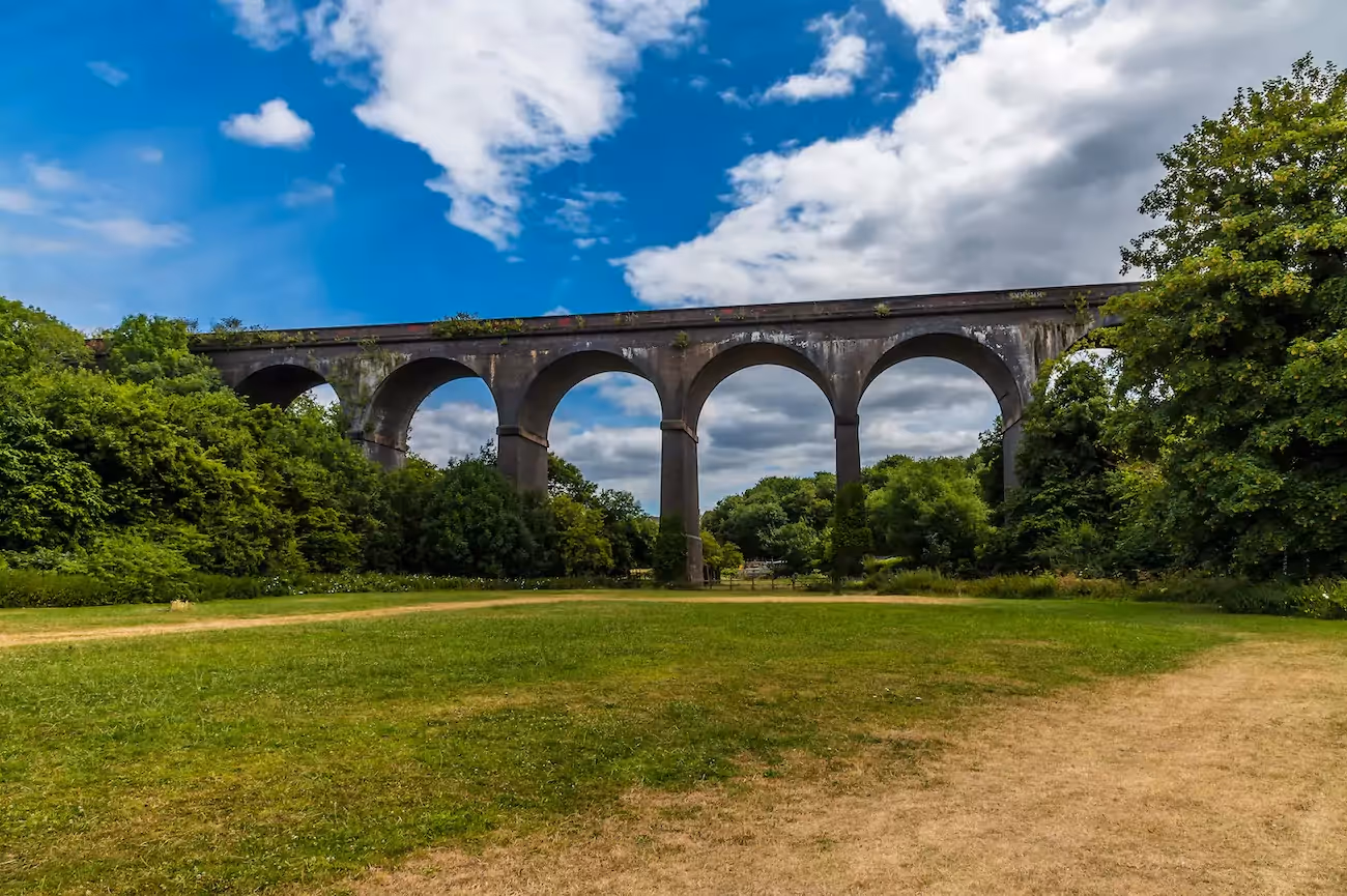 Victorian viaduct sitting over a field surrounded by trees on a sunny day