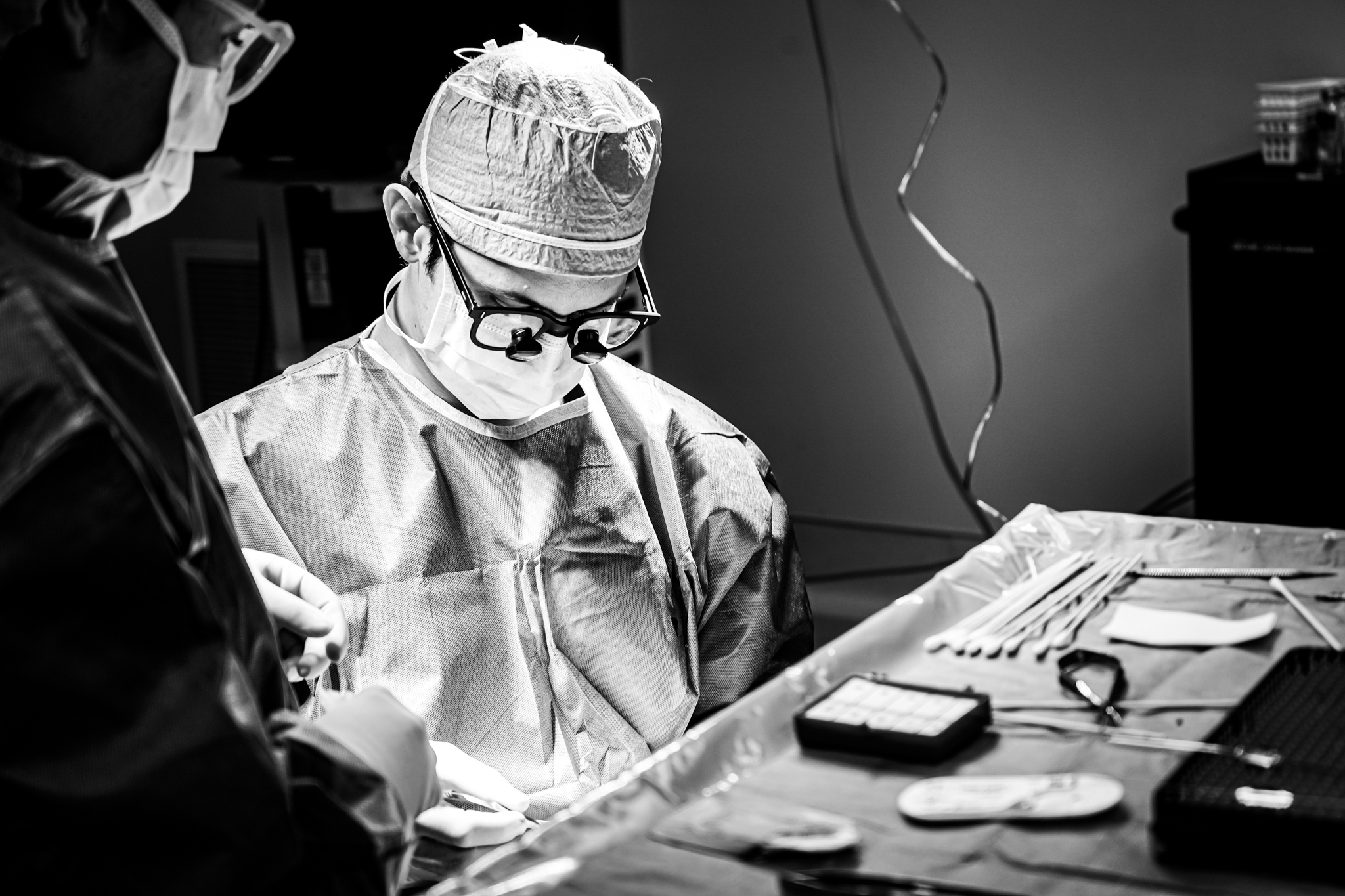 Surgeons wearing masks and protective gear performing an operation in a sterile operating room with surgical instruments laid out on a table.