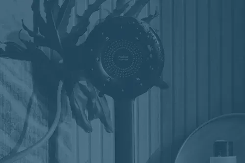 Contemporary black showerhead against wooden panels and patterned wallpaper with green plant and bathroom accessories.