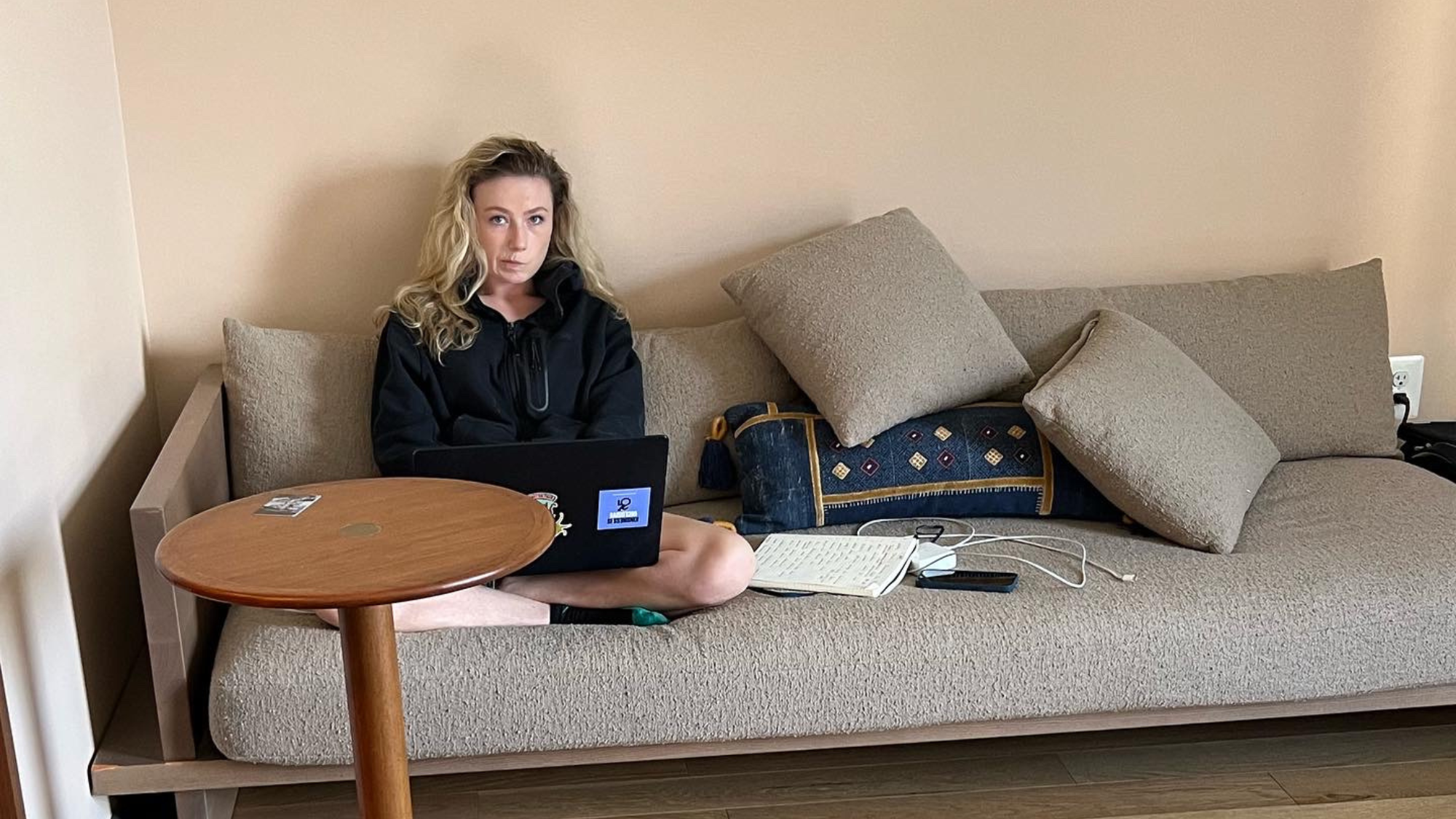 Picture of Keely sitting on a couch with her laptop and notebook strewn about. 