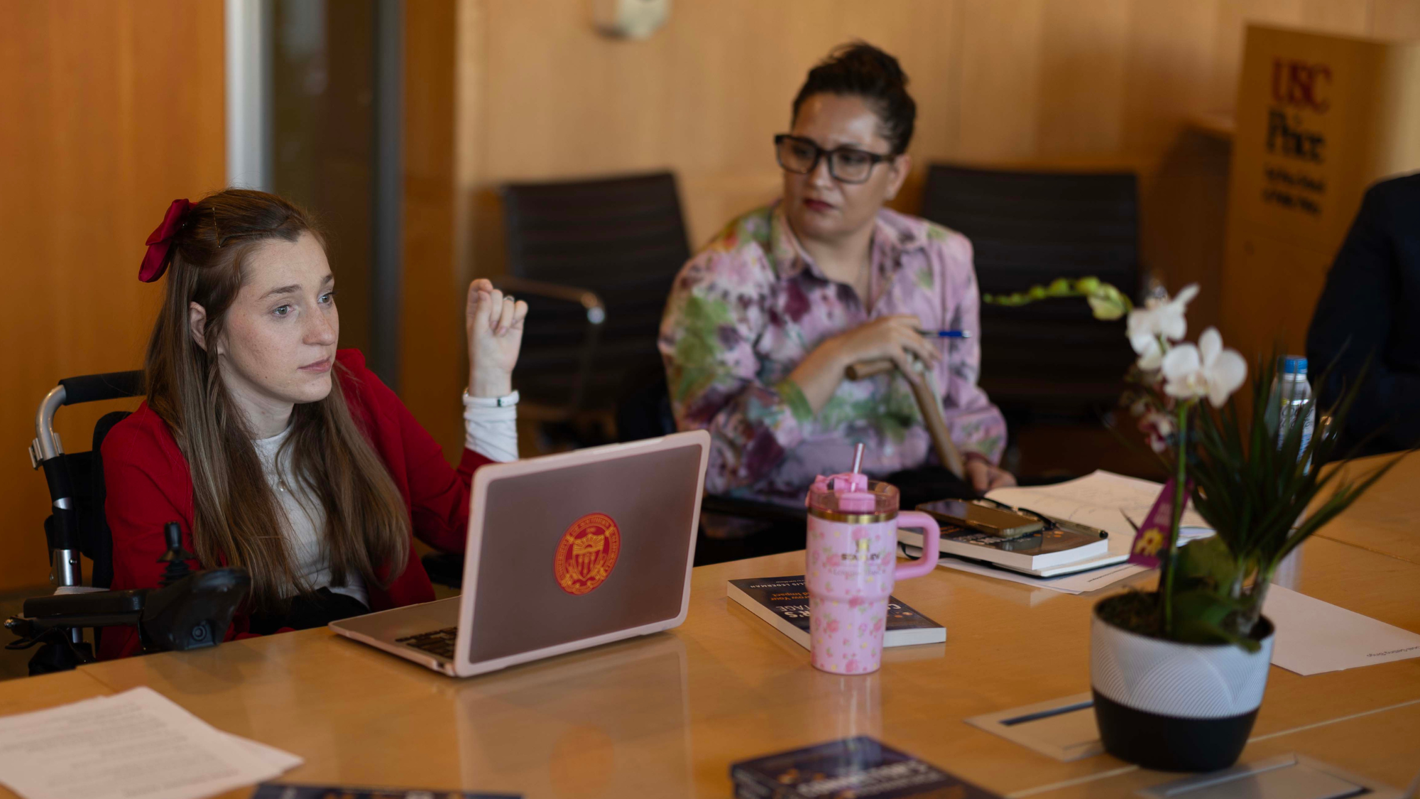 Making Space community members sit at a conference table engaged in discussion. One person is using a wheelchair and the other is sitting in a chair.