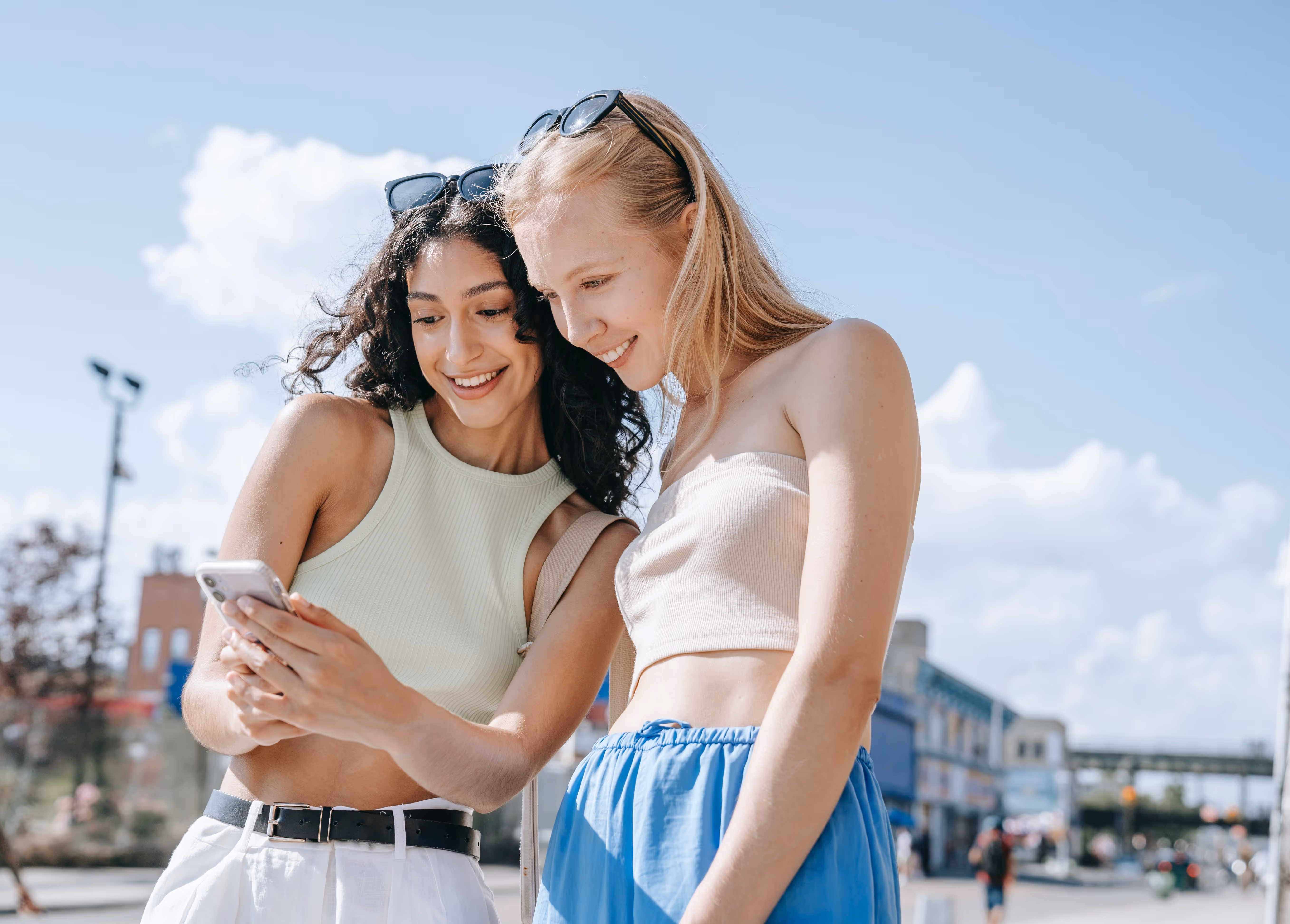 Two young women smiling and looking at a smartphone while walking outdoors, representing the vibrant lifestyle near Tessera in Los Angeles, CA.