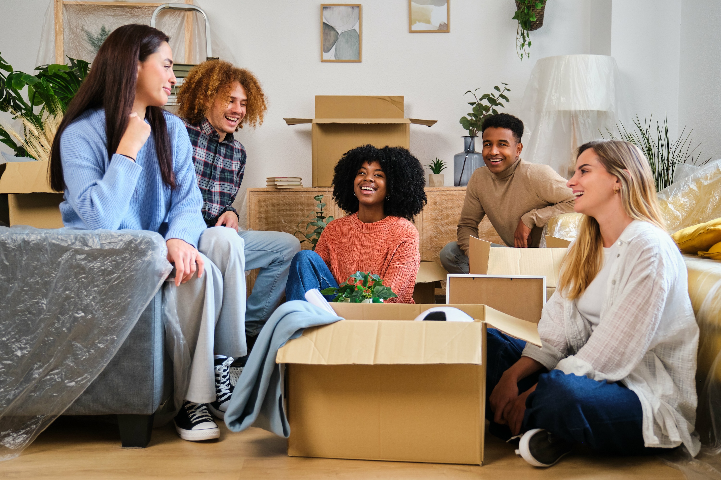 A group of five young adults laughing while taking a break from unpacking moving boxes, representing the welcoming community at Tessera in Los Angeles, CA.