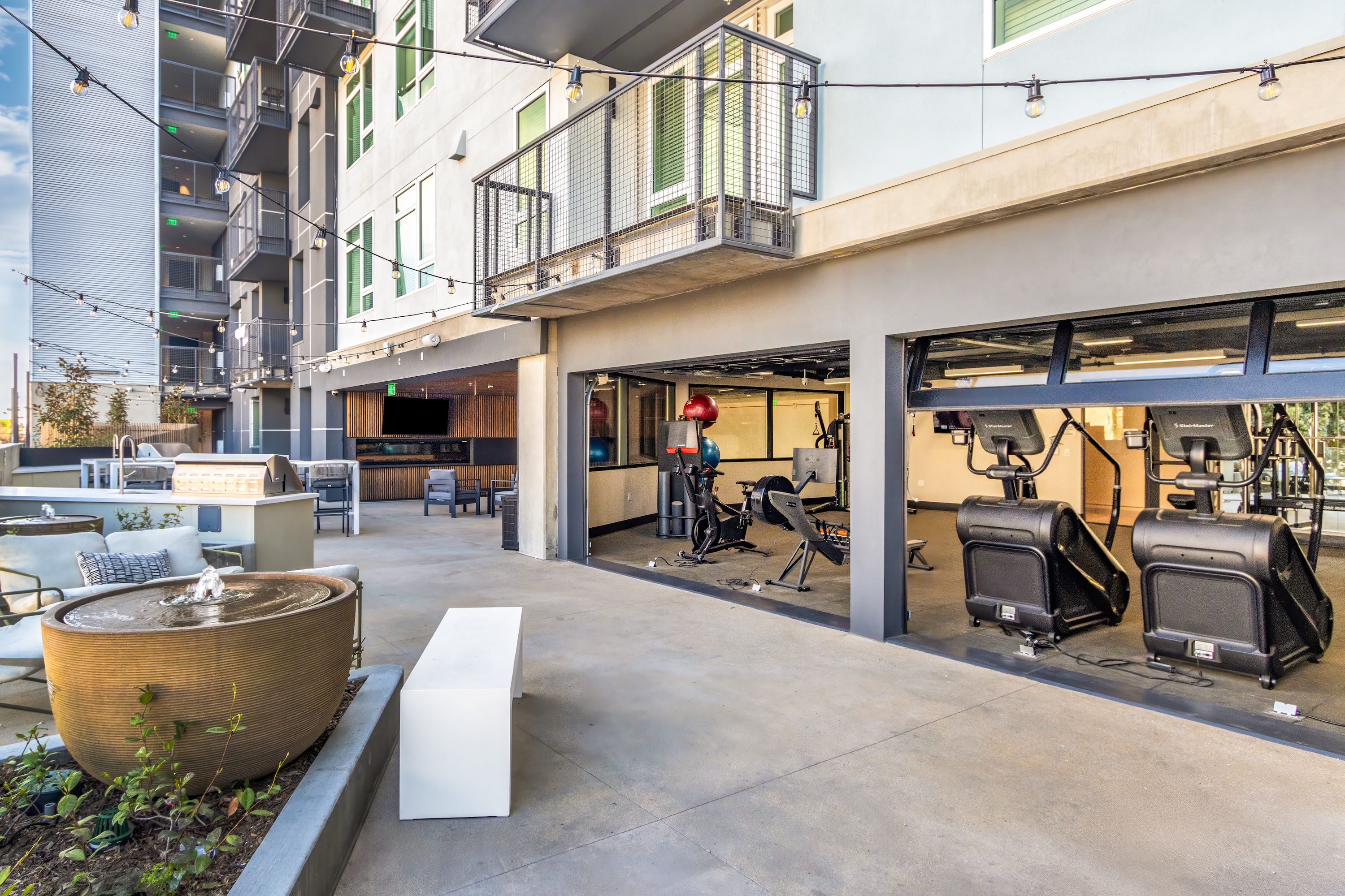 Rooftop amenity deck with a grilling station, bar seating, and festive string lights, showcasing the social scene at Tessera in Los Angeles, CA.