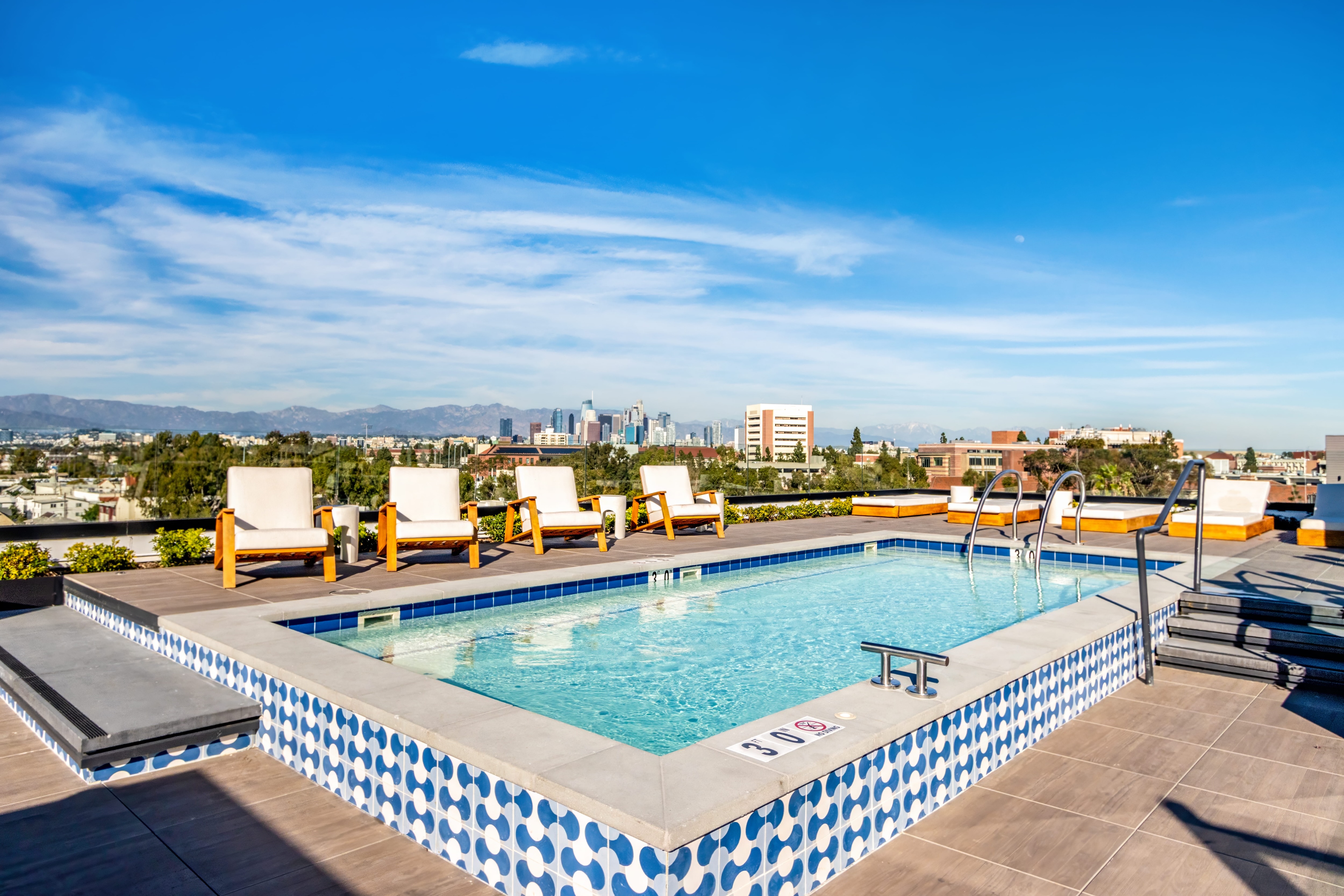 Rooftop swimming pool with a sundeck, lounge chairs, and views of the city skyline, offering a relaxing amenity at Tessera in Los Angeles, CA.