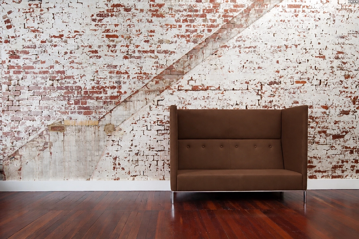 Blurred person walking past a modern red sofa against a white brick wall with diagonal brick pattern.