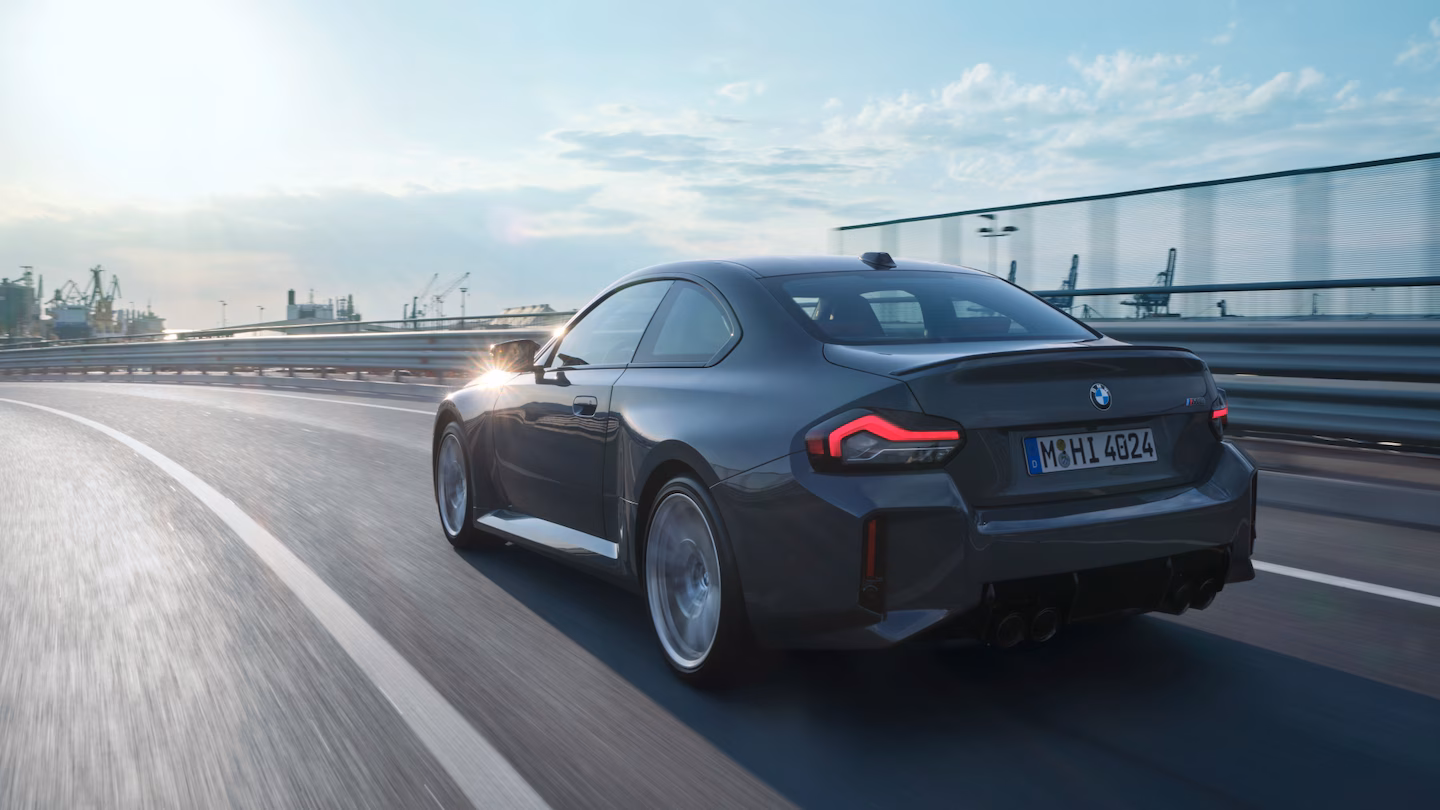 Schwarzer BMW M2 fährt schnell auf Kurvenstraße bei Sonnenuntergang.