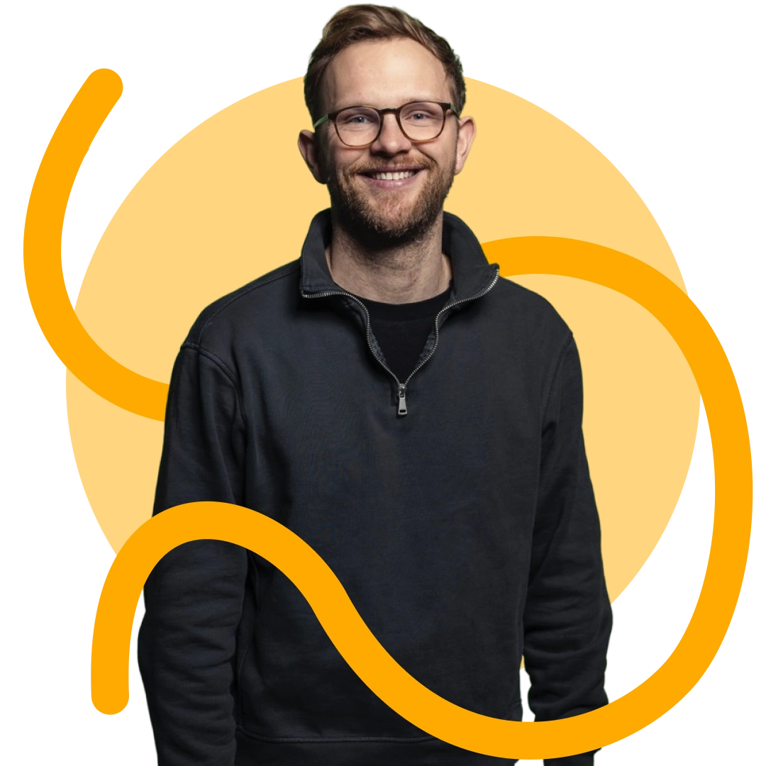 Junger Mann mit Brille und kurzem Haar, lächelnd in einem schwarzen Pullover vor einem gelben Hintergrund mit orangefarbenen geschwungenen Linien.