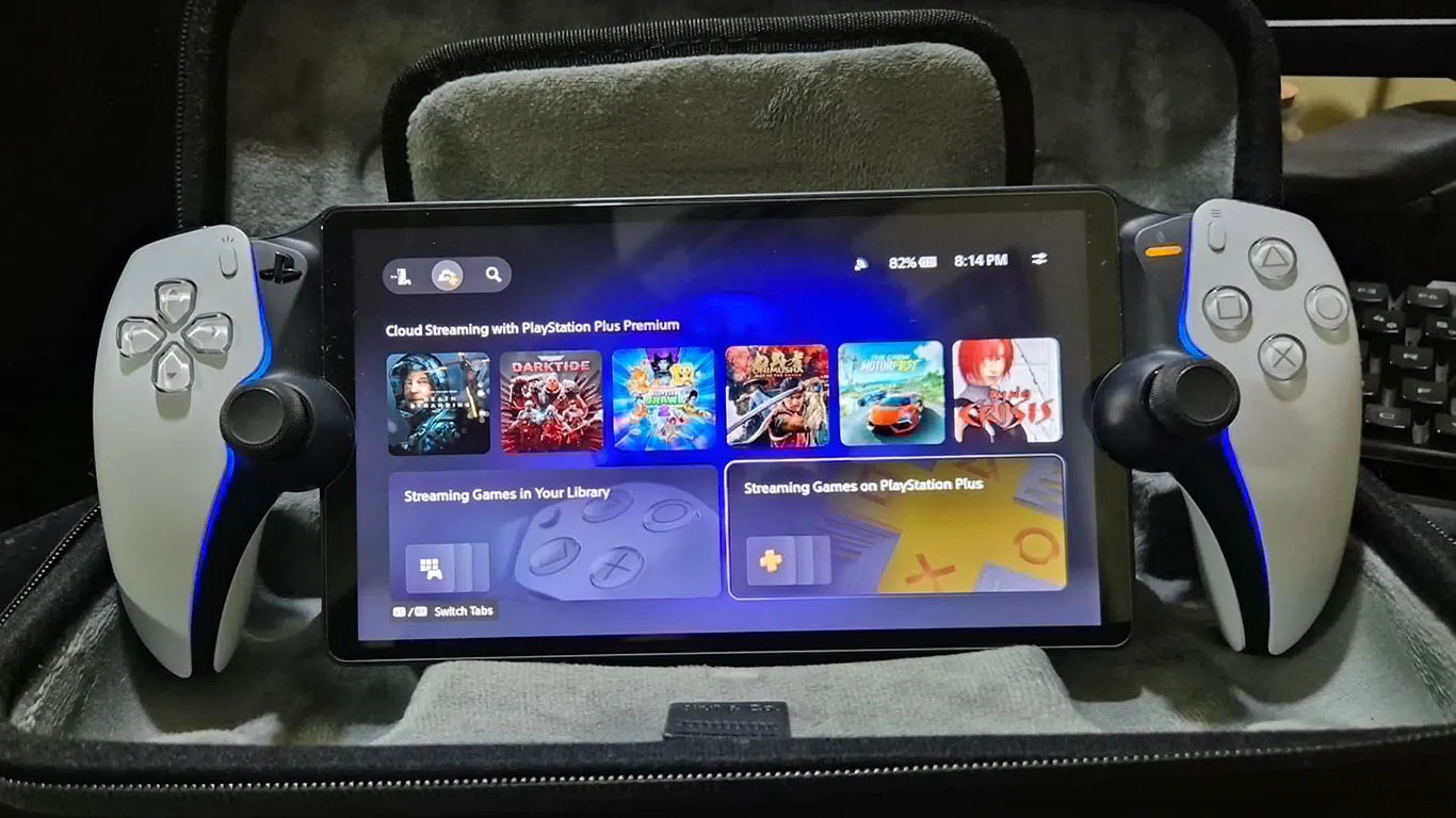 A PlayStation Portal handheld device with its 8-inch screen glowing and white DualSense-style grips, resting on a cozy bed with soft ambient lighting in a gamer's bedroom.