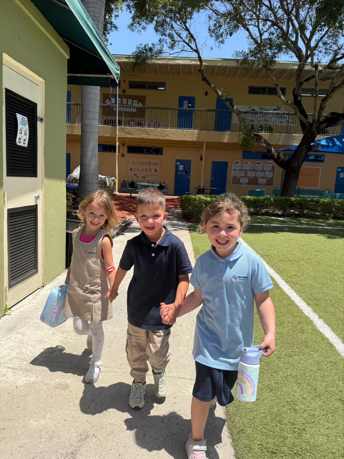 Three Gordon Day School students smiling and holding hands as they walk across campus