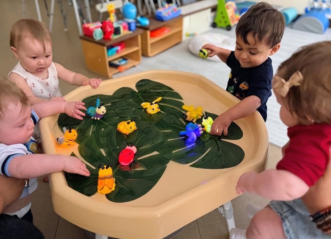 Infants and toddlers gathered around a sensory table playing with glowing bug toys