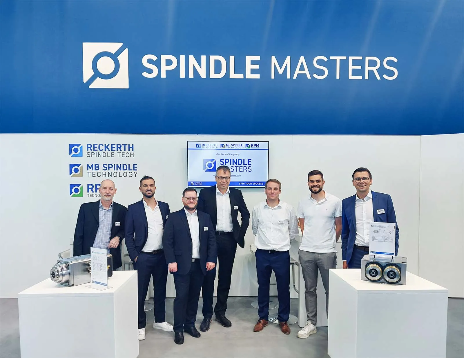 Das Gruppenfoto zeigt die verantwortlichen Personen der Spindle Masters an einem Messestand mit verschiedenen Spindlelösungen