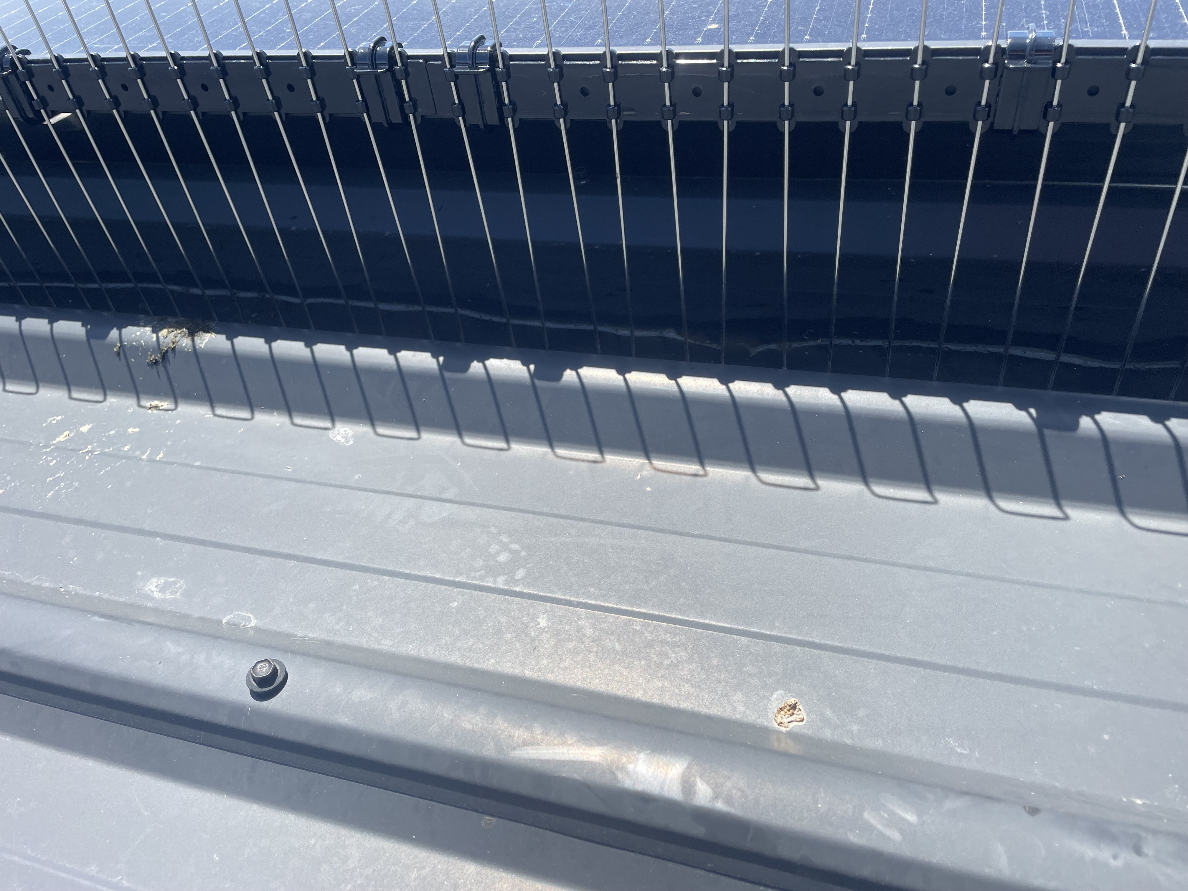 Close-up of rooftop with solar panels and a metal surface showing dirt, bolt, and a small hole.