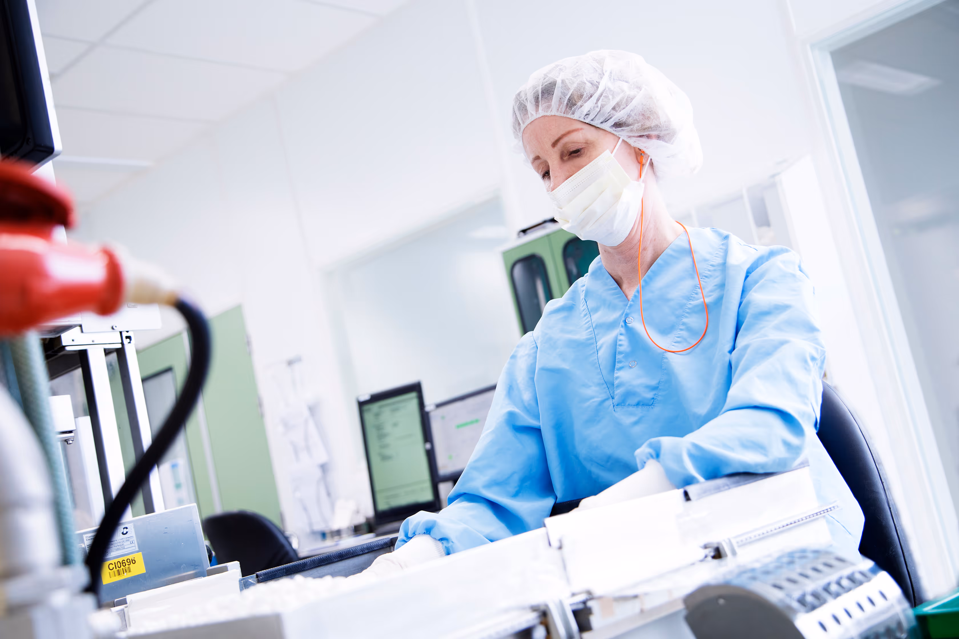 Healthcare worker in blue scrubs and protective gear operating medical or laboratory equipment.