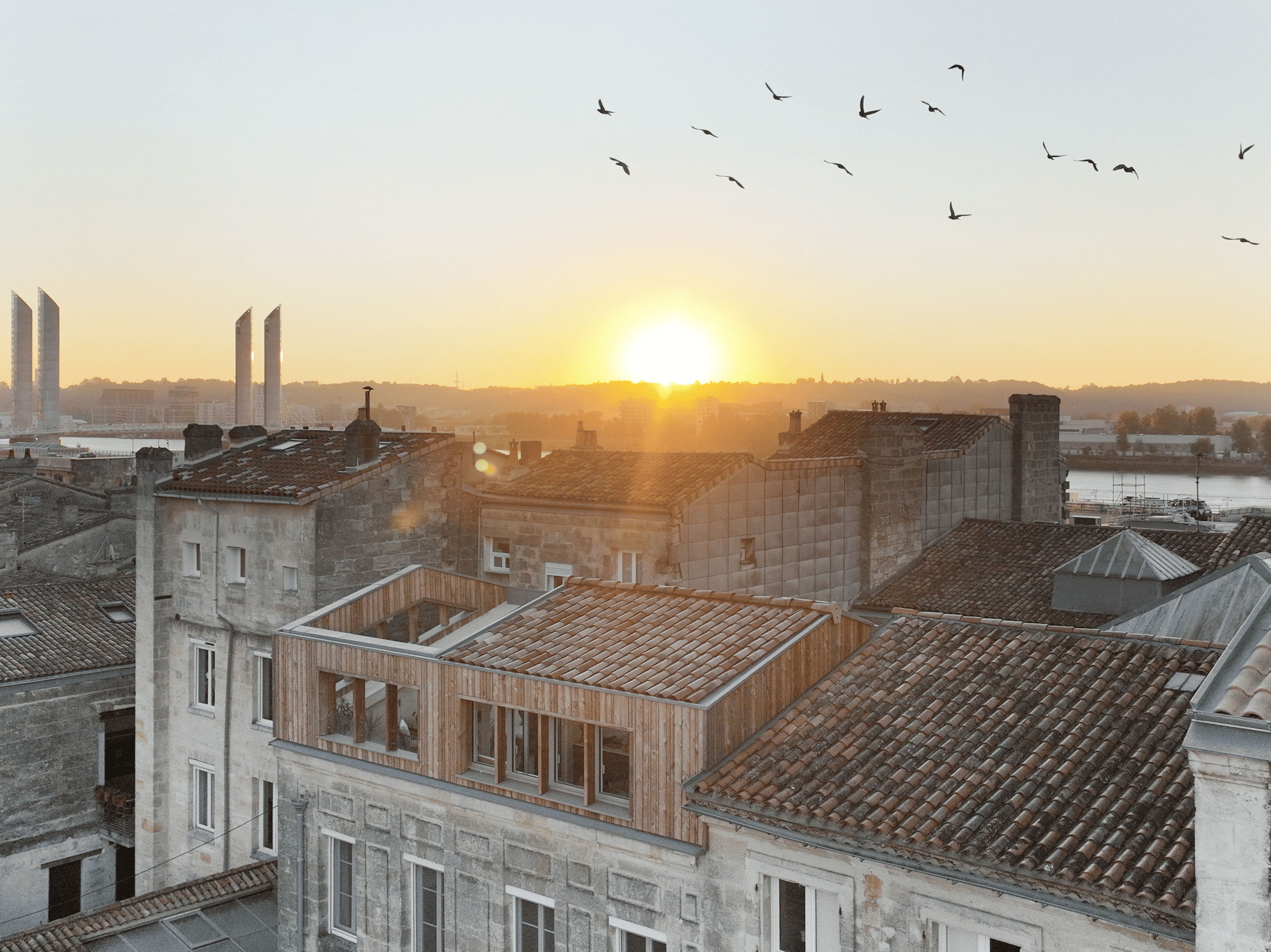 Vue aérienne au coucher du soleil de la surélévation bois HEDLO sur les toits des Chartrons, pont Chaban-Delmas au loin